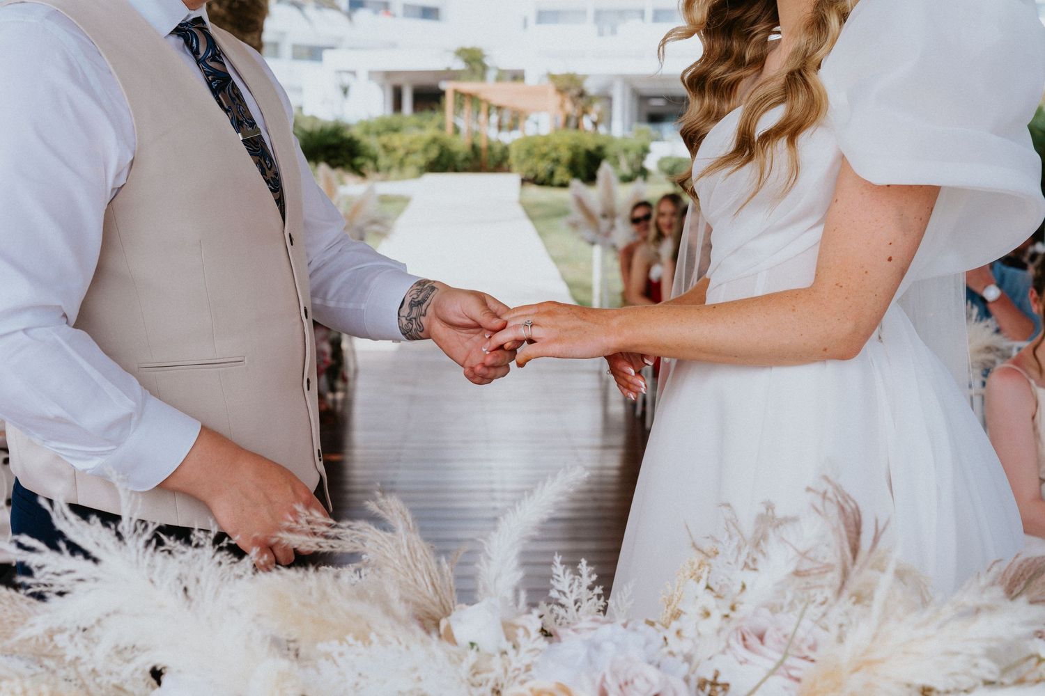 Close-up of couple exchanging wedding rings during beachside ceremony decorated with dried pampas grass.