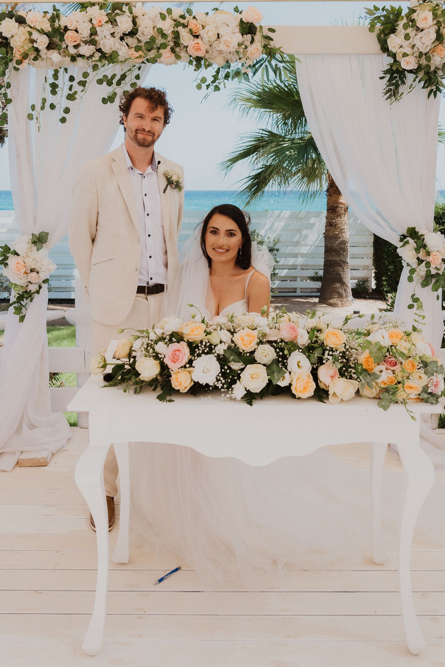 Newlyweds at signing table decorated with lush floral arrangements and white drapery.