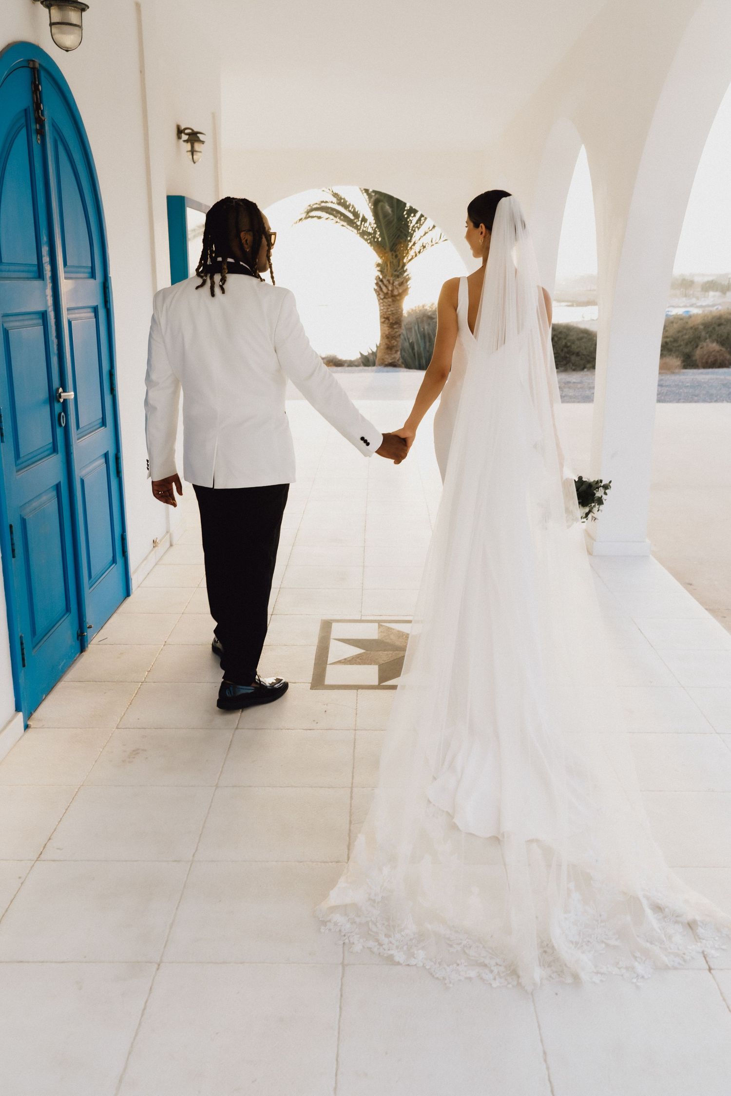 Couple walking through Mediterranean archway with blue door and palm trees.