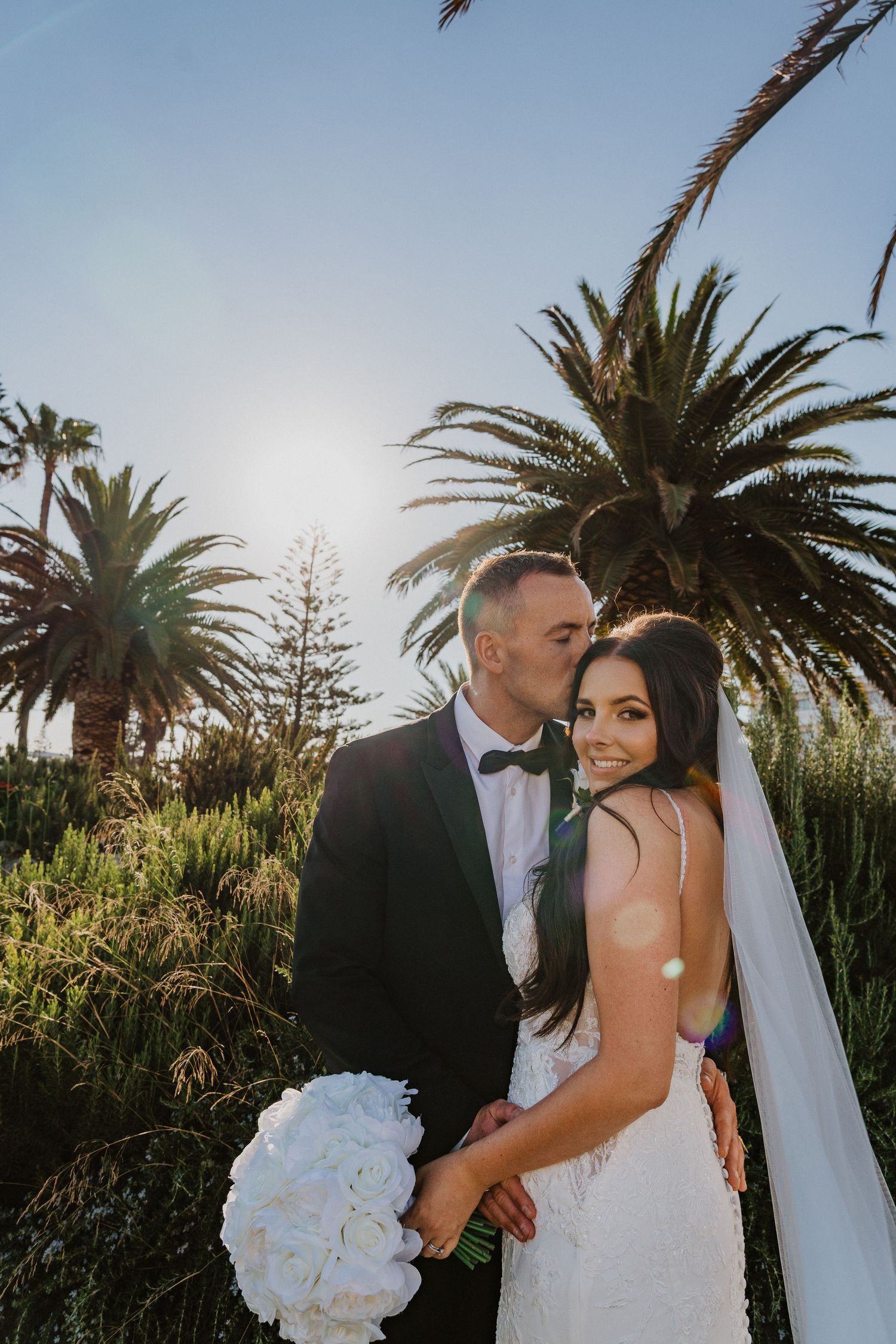 Tropical garden wedding portrait with palm trees and white bouquet at golden hour.