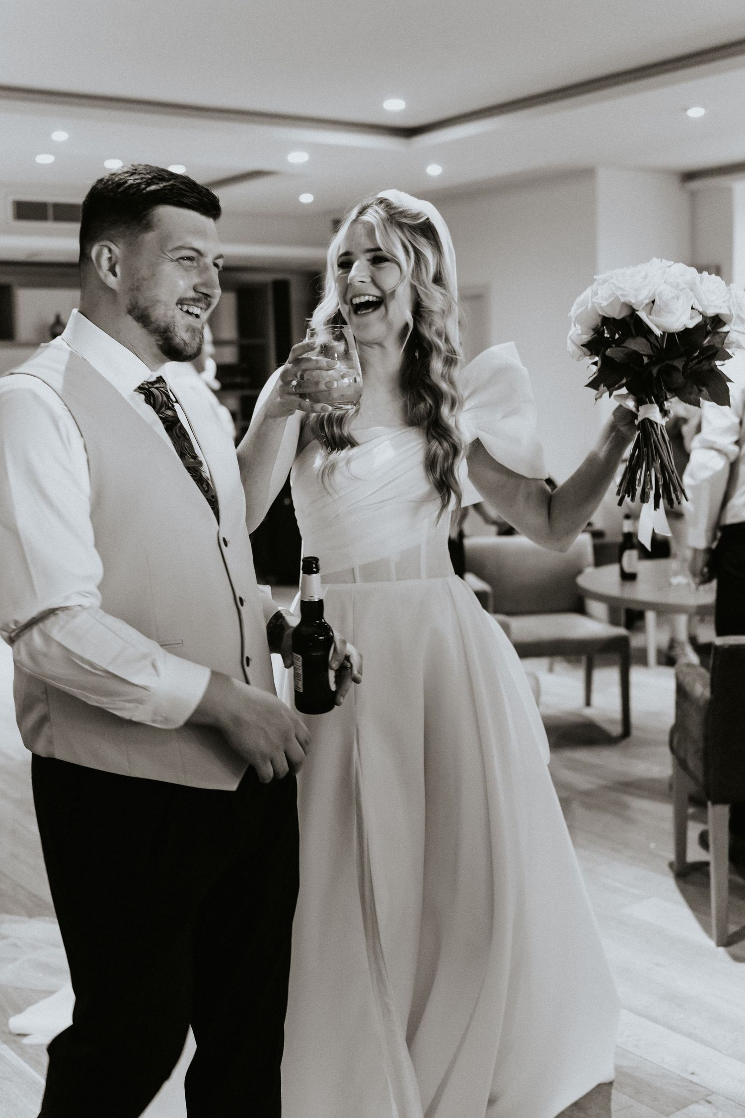 A candid black and white wedding photo shows a bride and groom laughing together during their celebration.