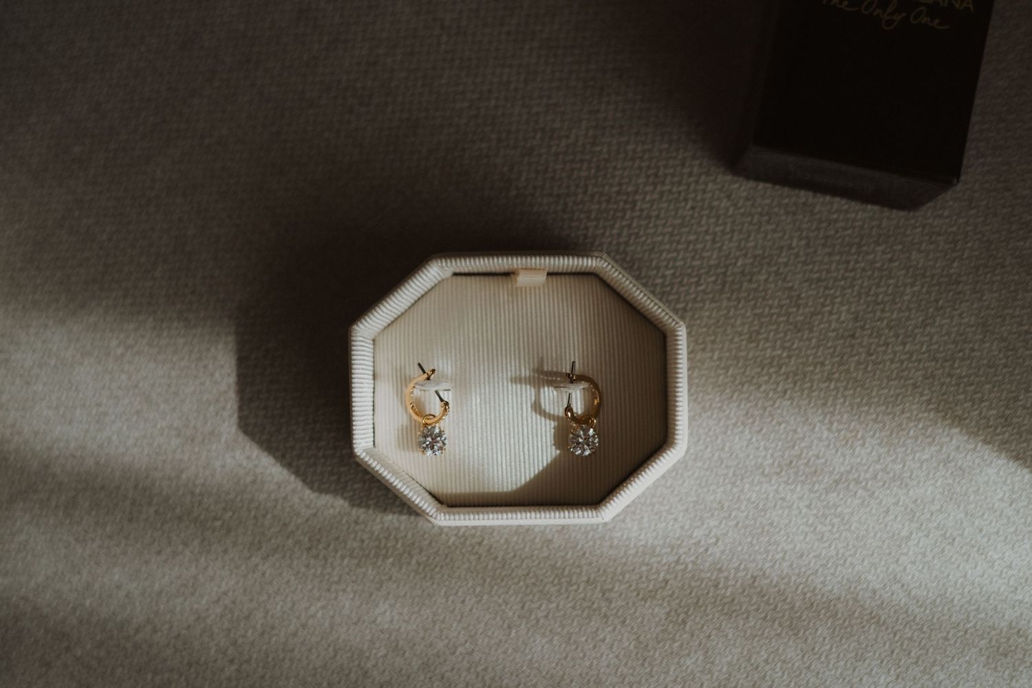 Delicate wedding jewelry displayed in an octagonal box on a textured surface.
