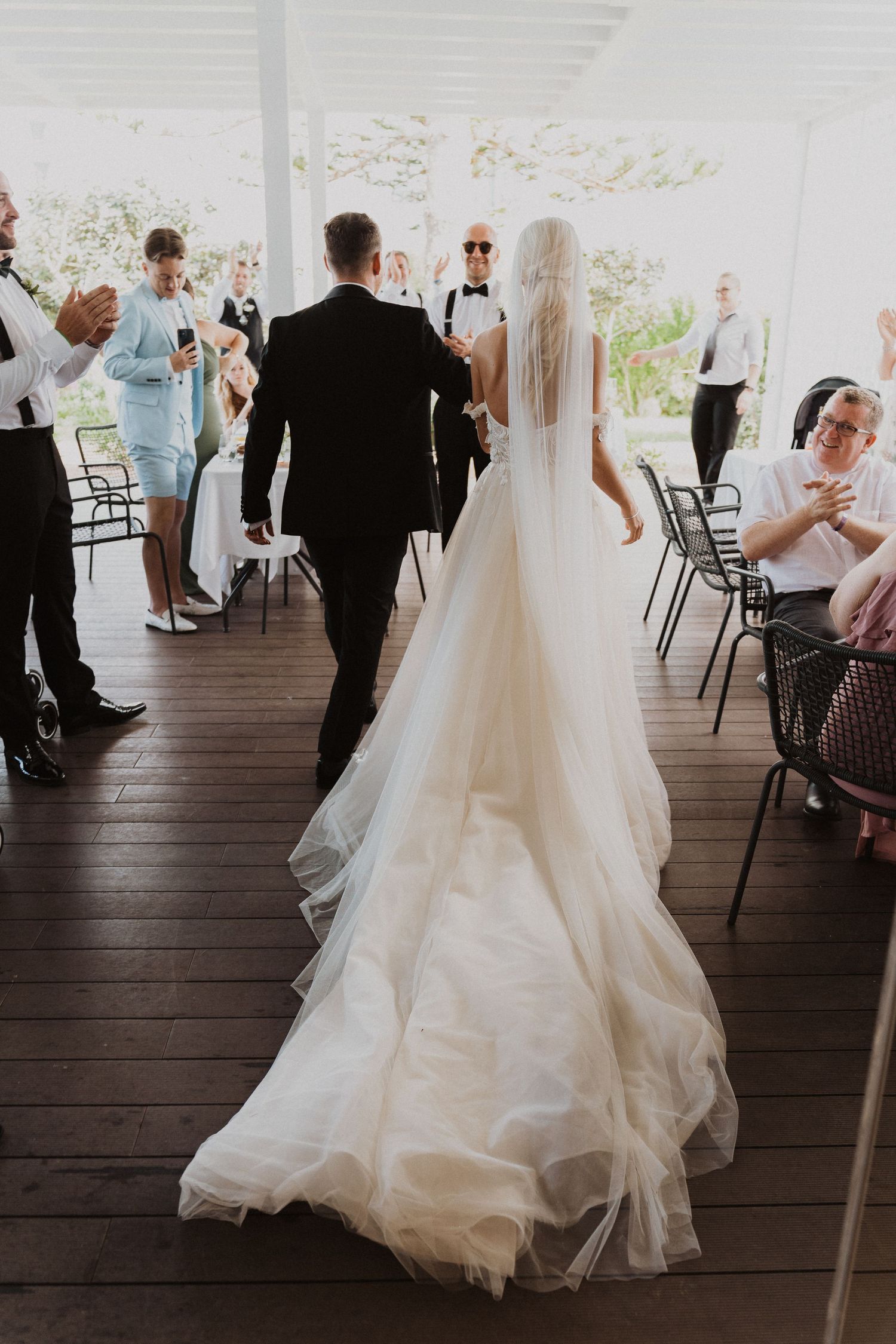 Wedding ceremony exit with guests applauding on covered outdoor deck.