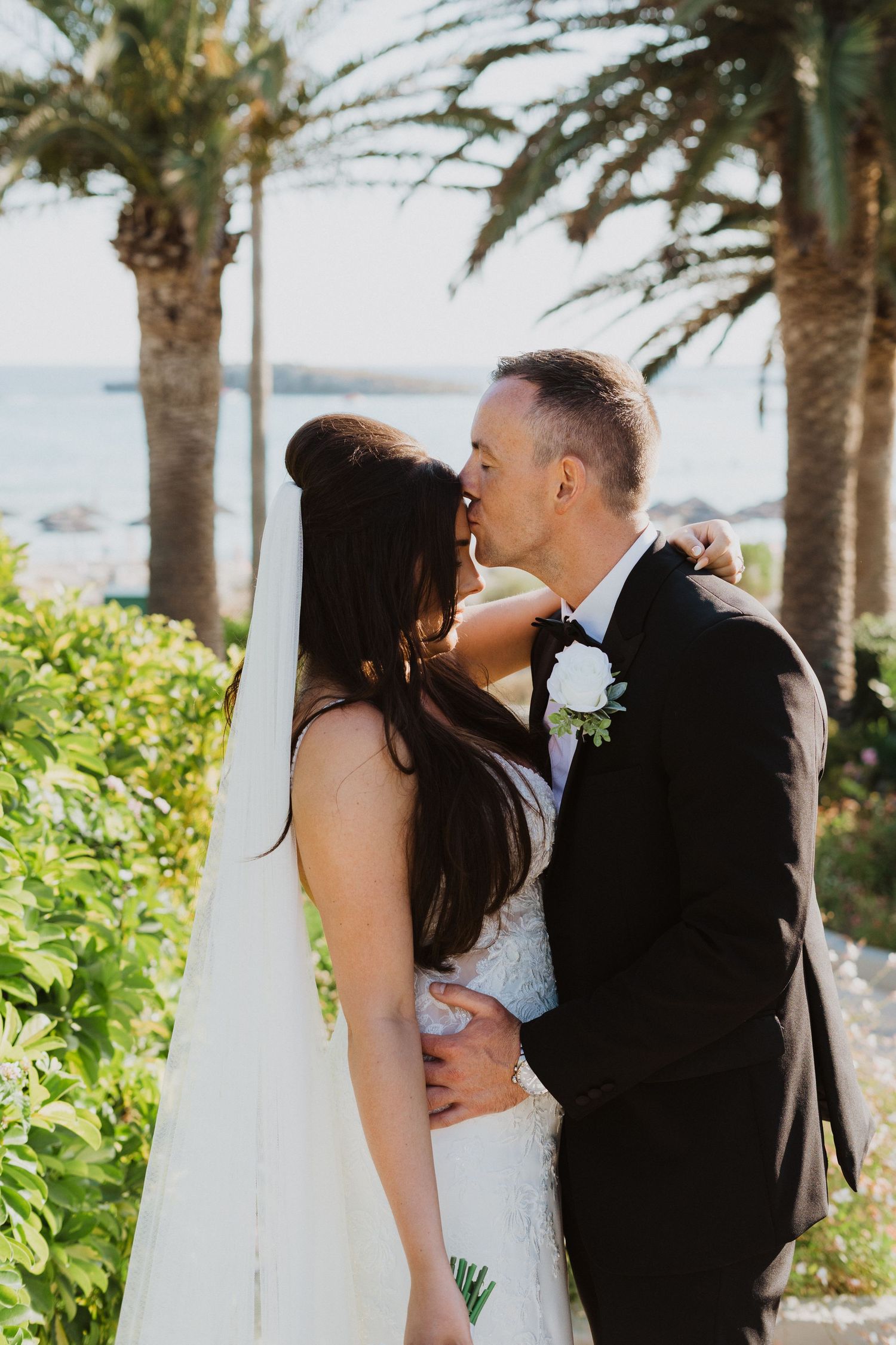 An intimate wedding moment shared between a couple in a palm-lined garden.