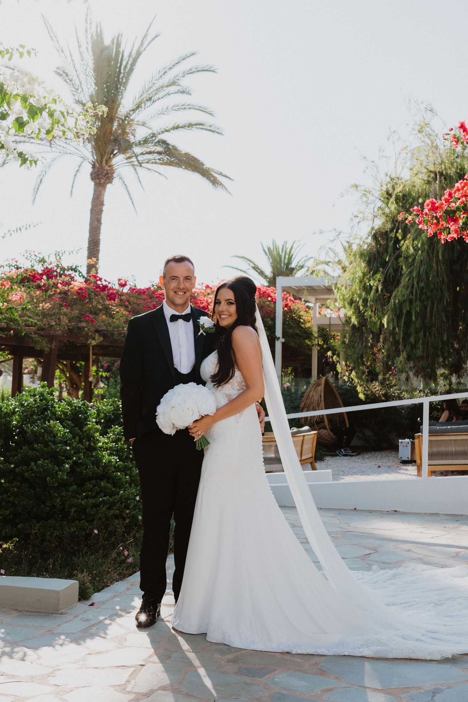 Wedding couple poses for romantic photos on a stone pathway with palm trees and bougainvillea.