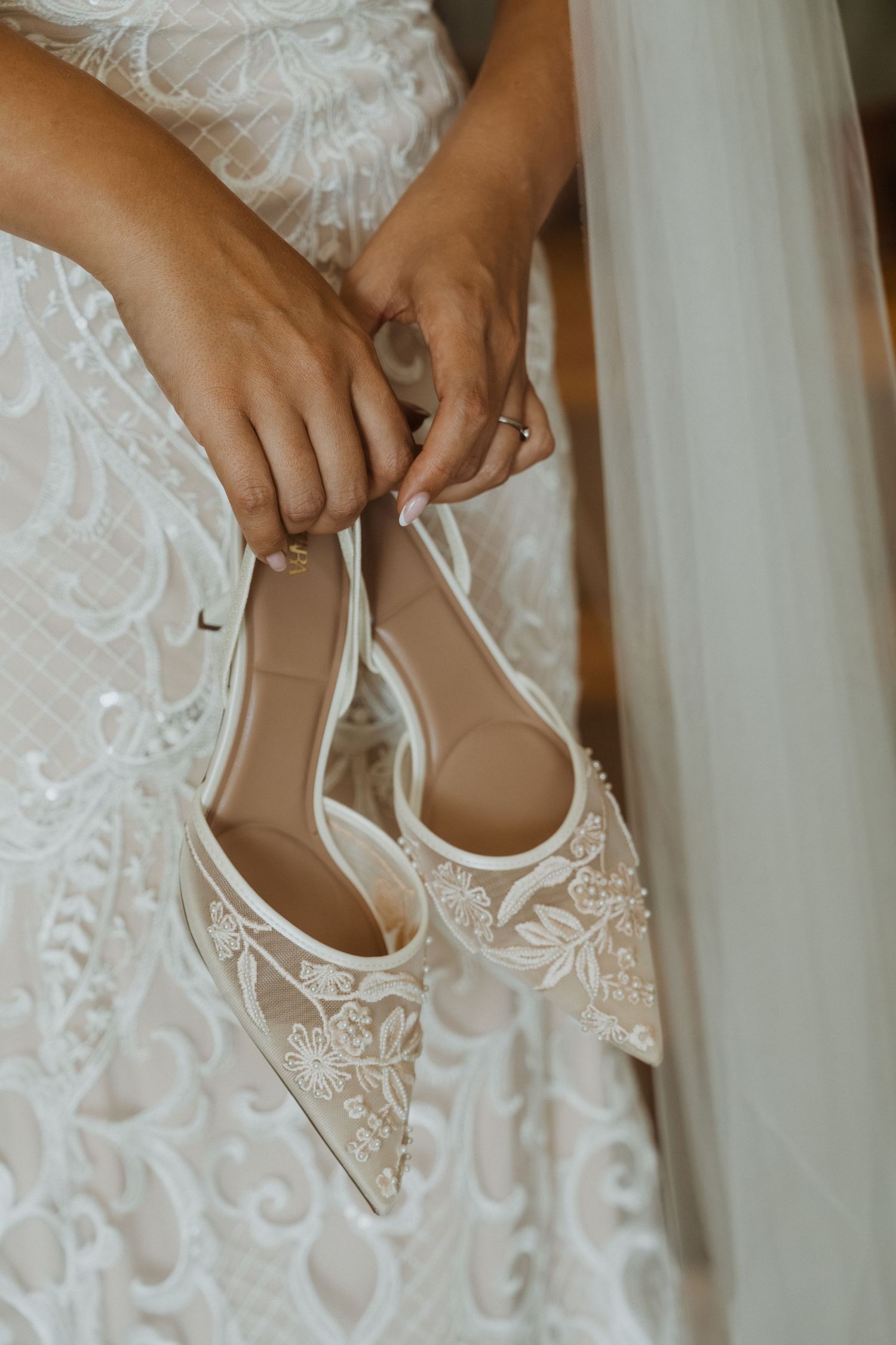 Close-up view of hands holding elegant white lace wedding shoes with delicate embroidered details.