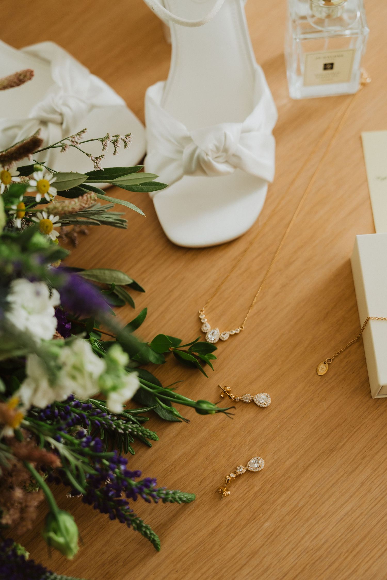Elegant bridal accessories with white shoes, flowers and jewelry on wooden surface.