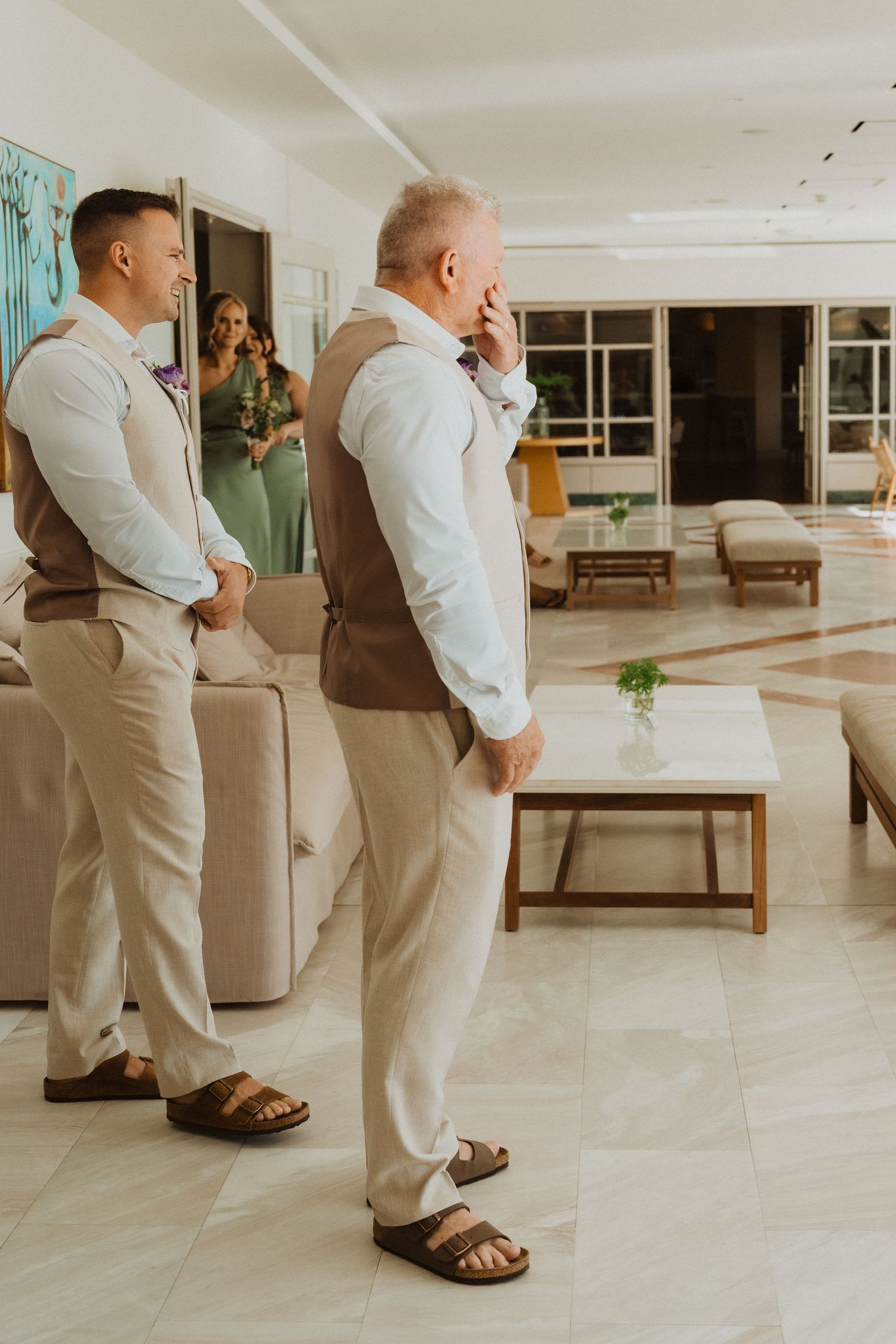 Wedding party members in beige suits pose informally in a modern indoor setting.