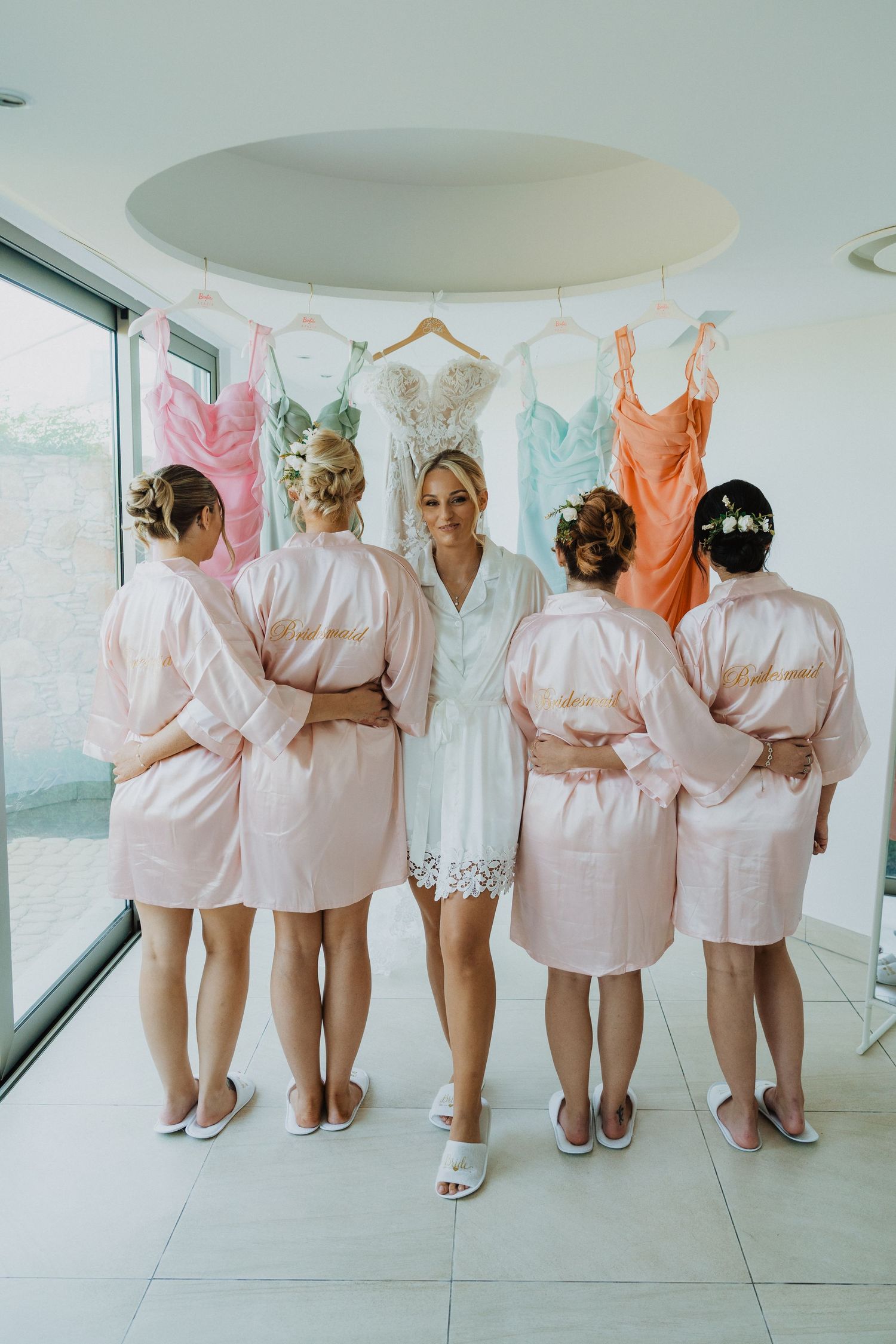 Wedding party members stand with their backs to the camera, showing off matching pink robes.