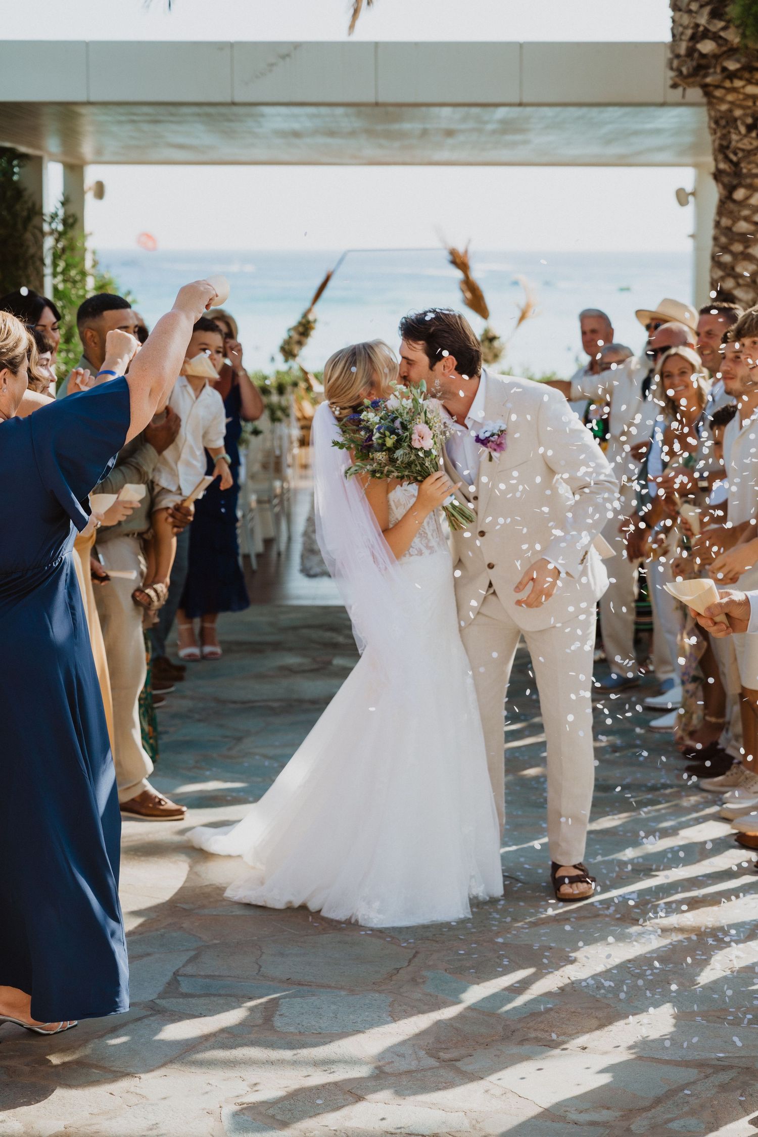 Beachside wedding exit with guests throwing confetti in afternoon sunlight.