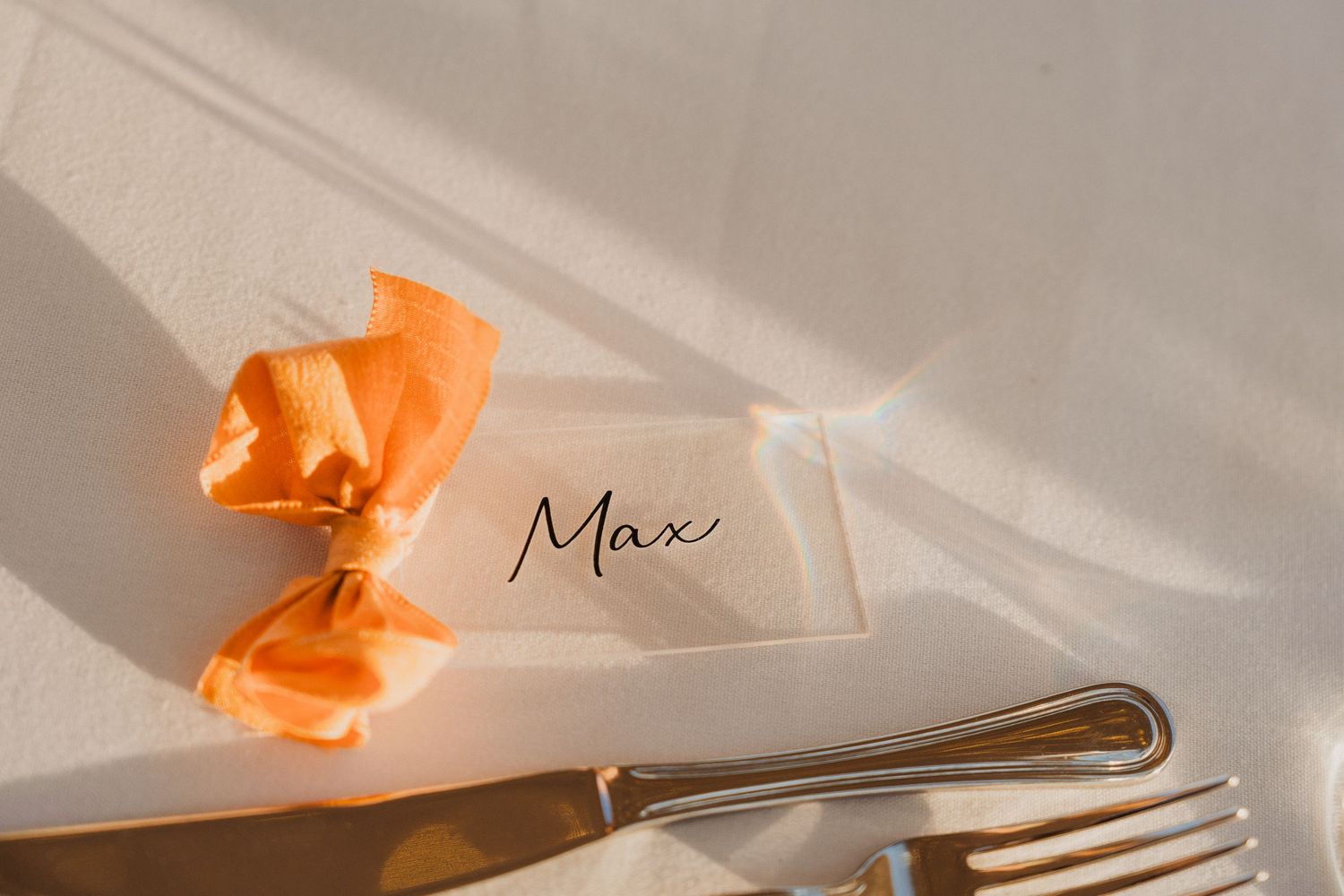 Place setting detail with peach bow and silverware on white linen.