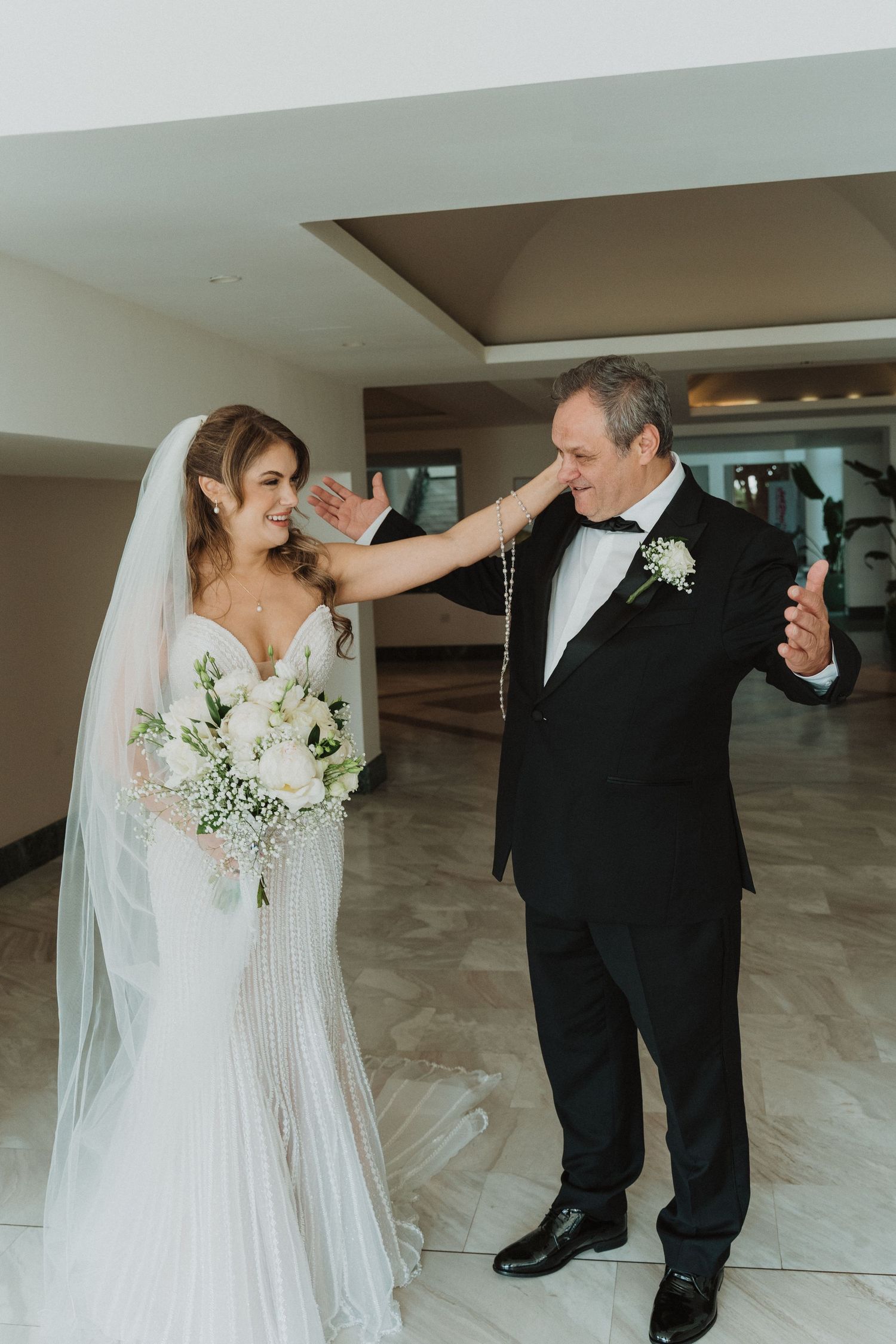 Emotional father daughter first look moment with bride in fitted gown holding white bouquet.