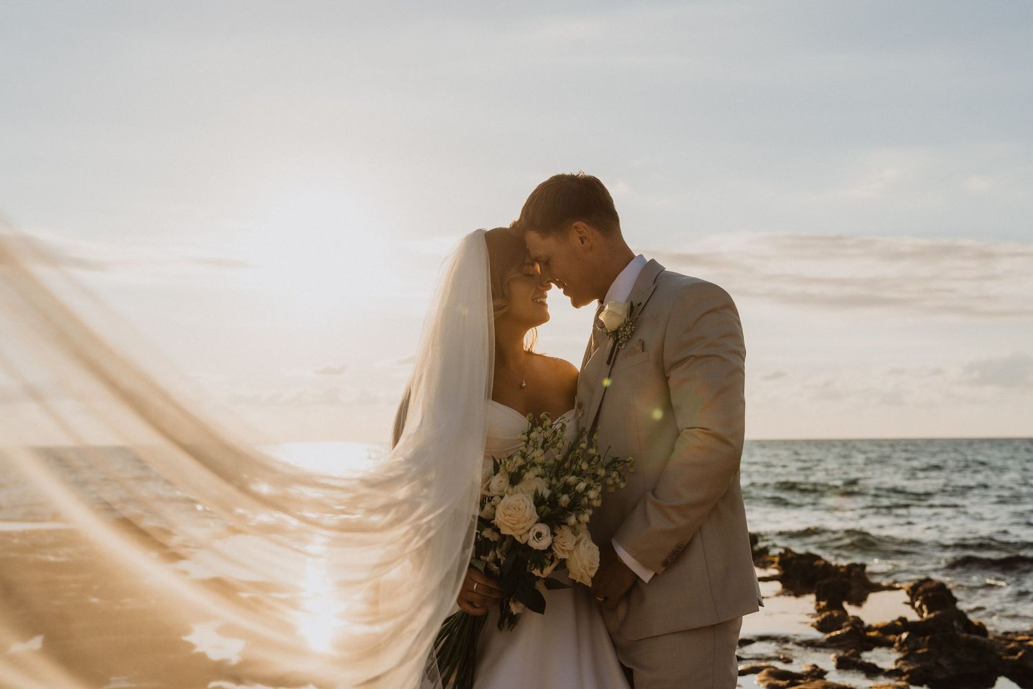 A romantic sunset beach wedding photo with a couple embracing as golden light streams across the ocean waves.