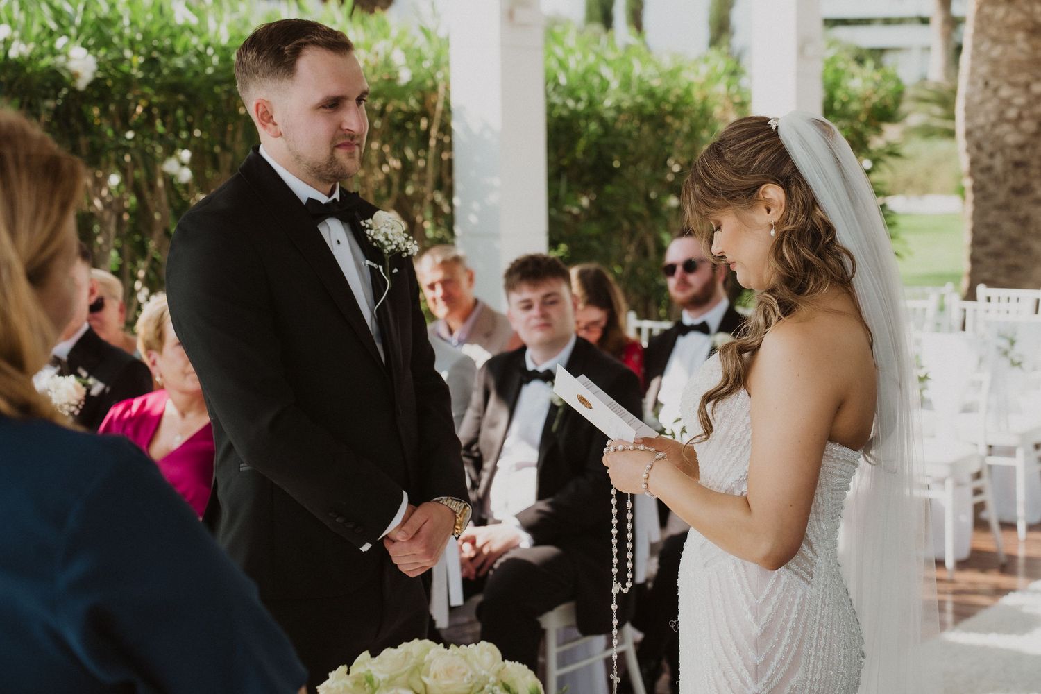 Bride reading wedding vows to groom during intimate outdoor ceremony with seated guests.