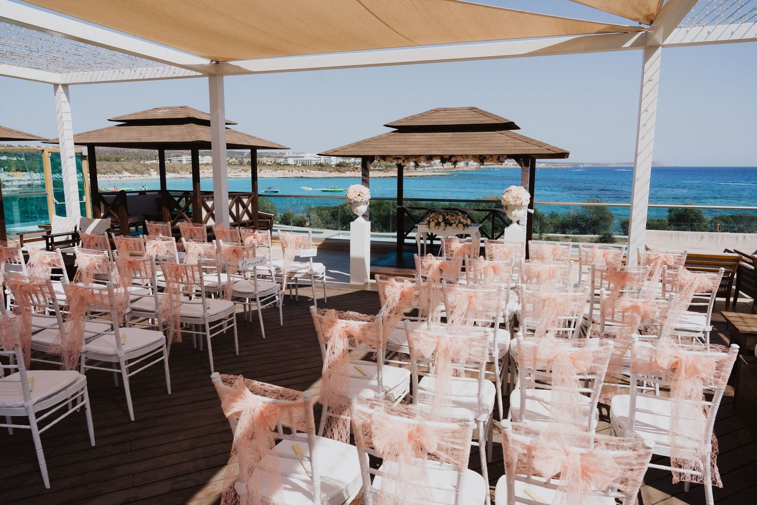 Wedding ceremony setup with white chairs and pink decor overlooking the Mediterranean sea.