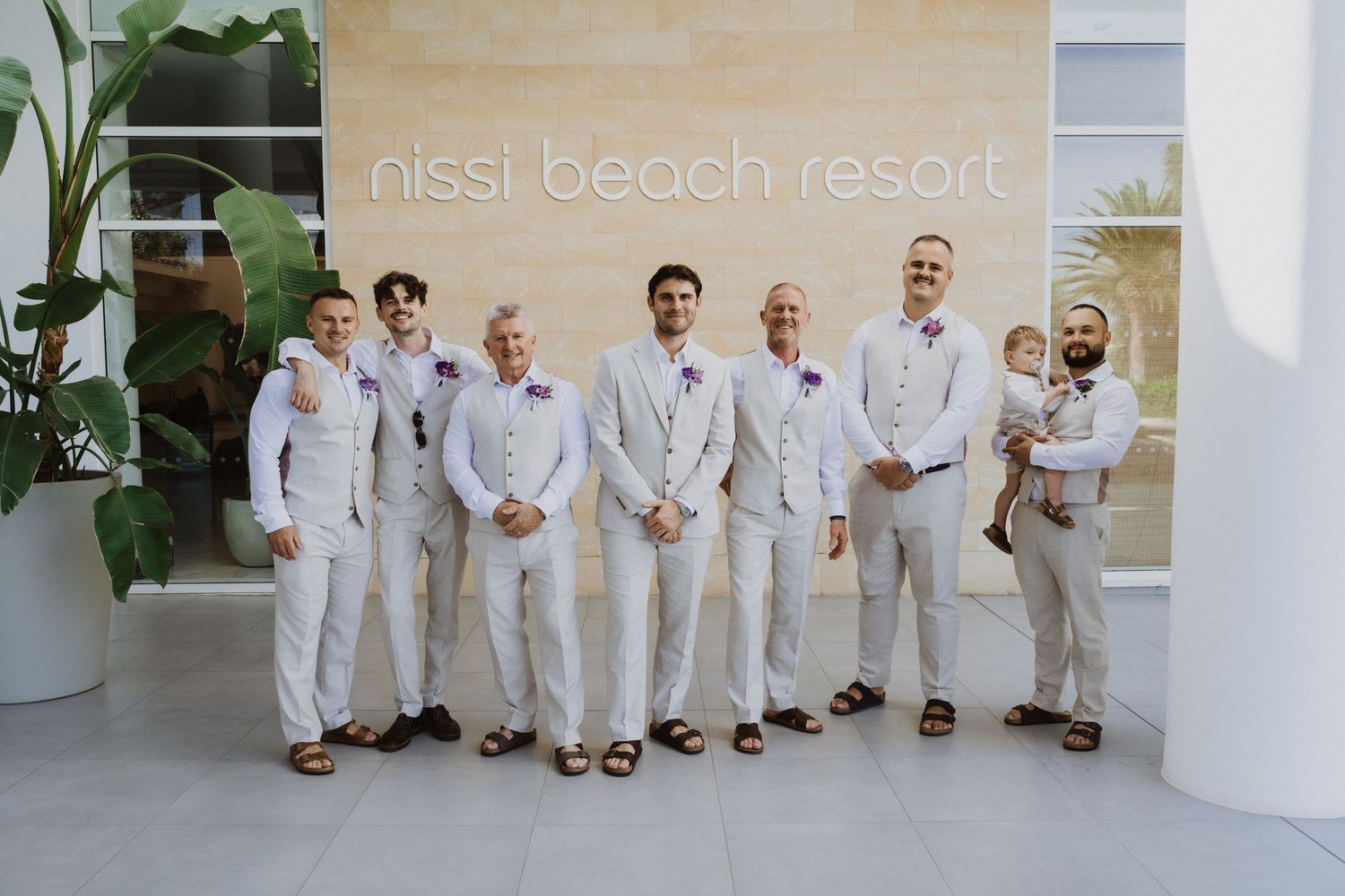 Groomsmen group photo at Nissi Beach Resort with modern architecture backdrop.