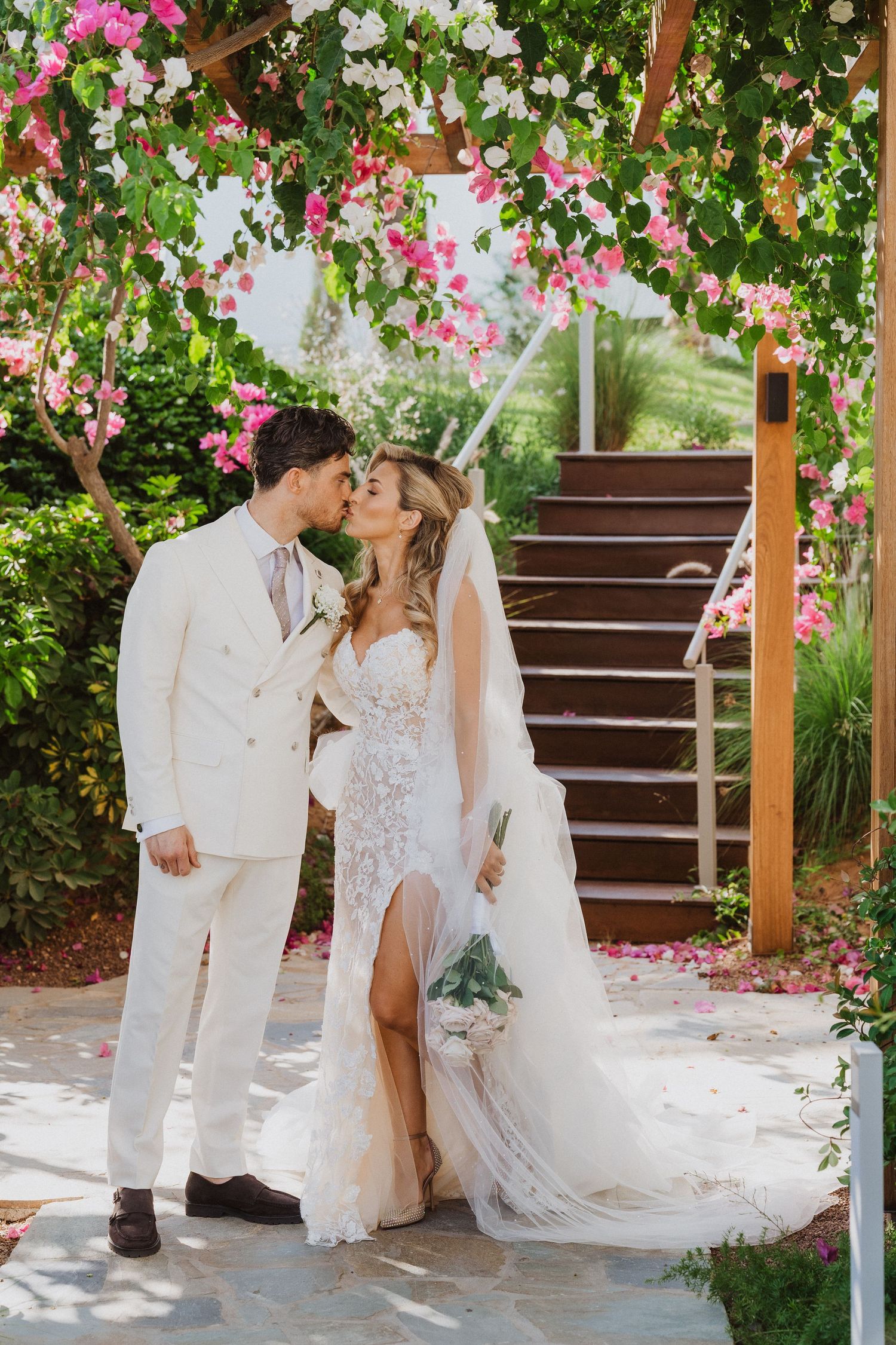 A couple shares a romantic moment under a floral arch with pink blooms and greenery on their wedding day.