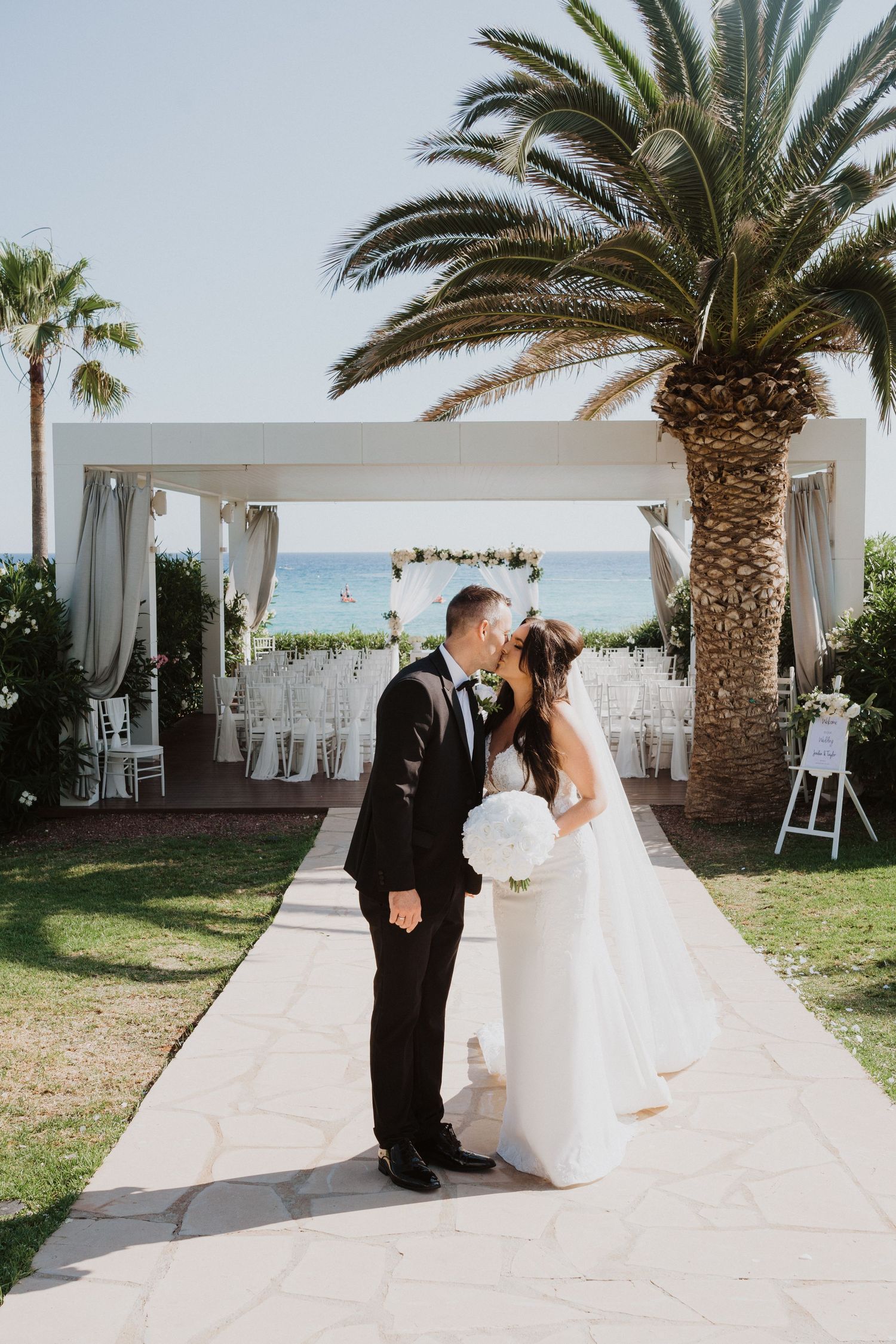 A couple shares a romantic moment under palm trees at an elegant outdoor wedding venue.