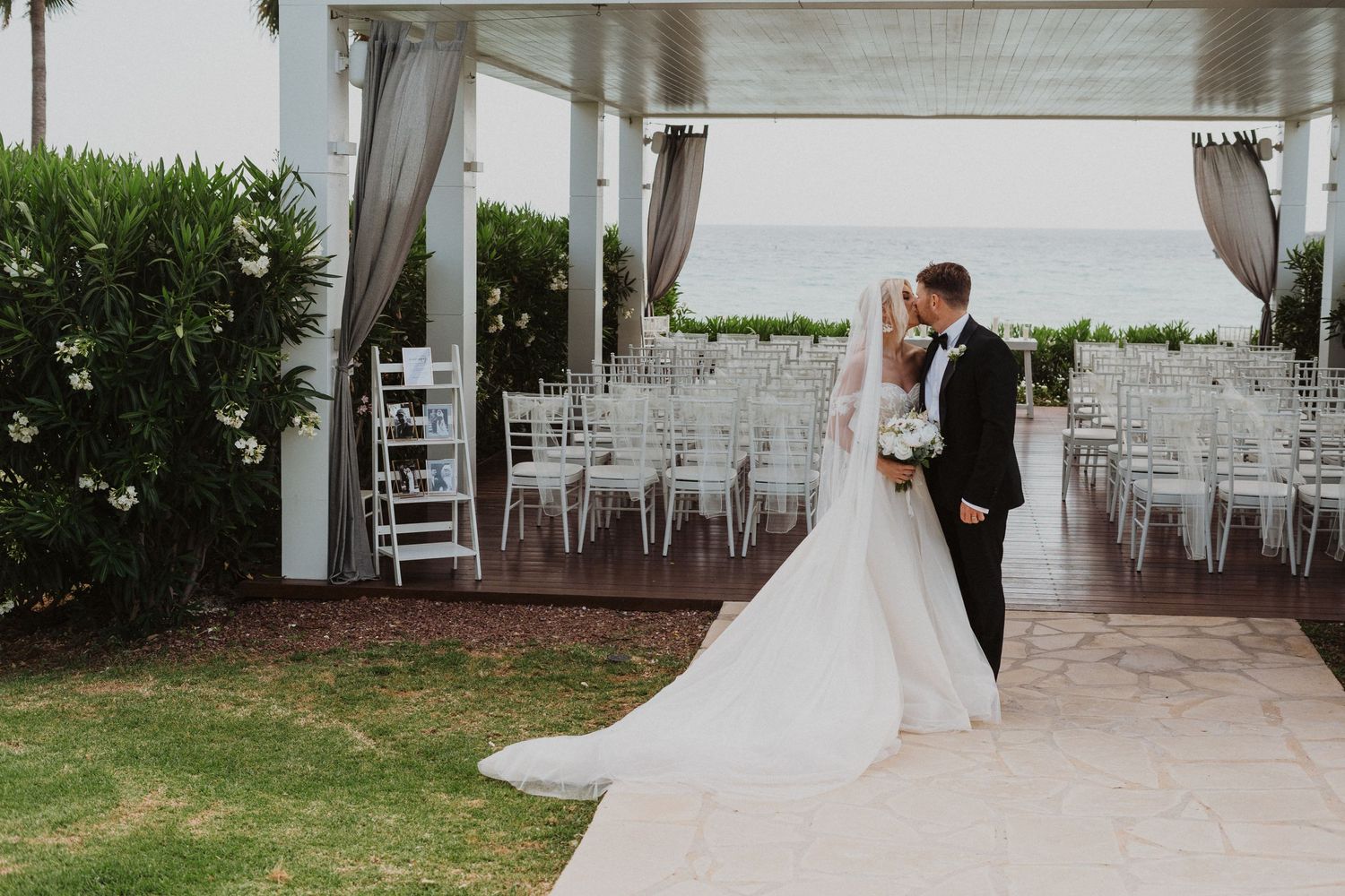 A romantic wedding moment captured under an elegant white pavilion with ocean views.