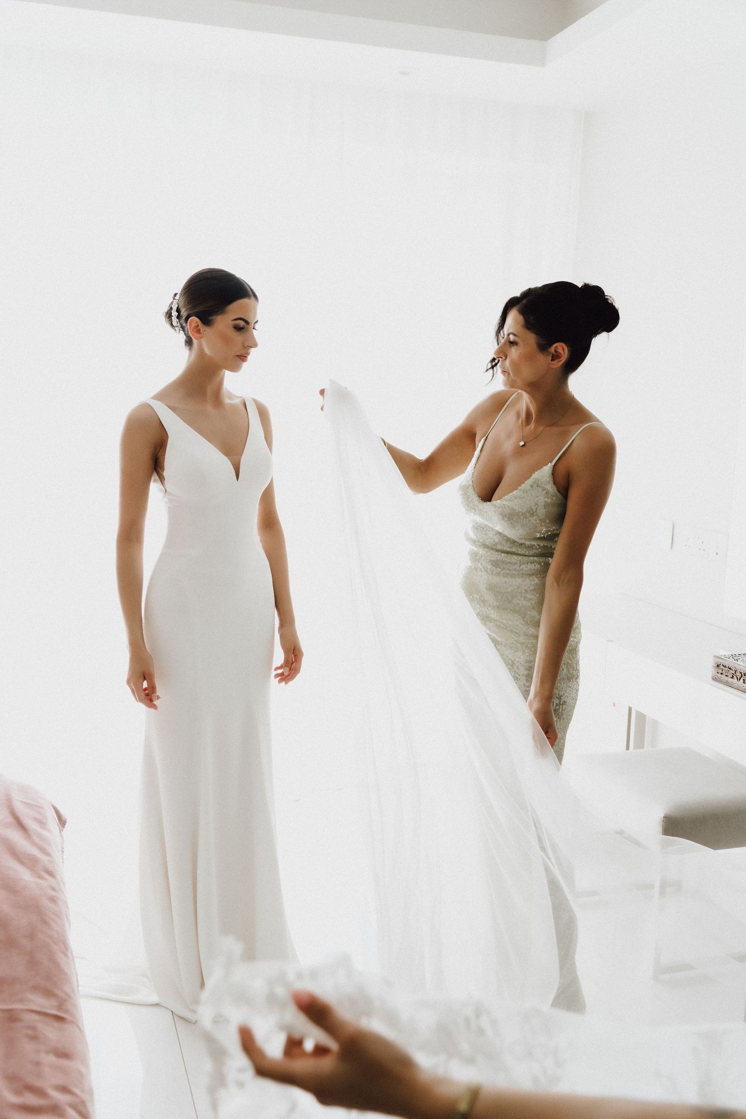 Bridal preparation scene showing two women in white dresses arranging wedding attire.