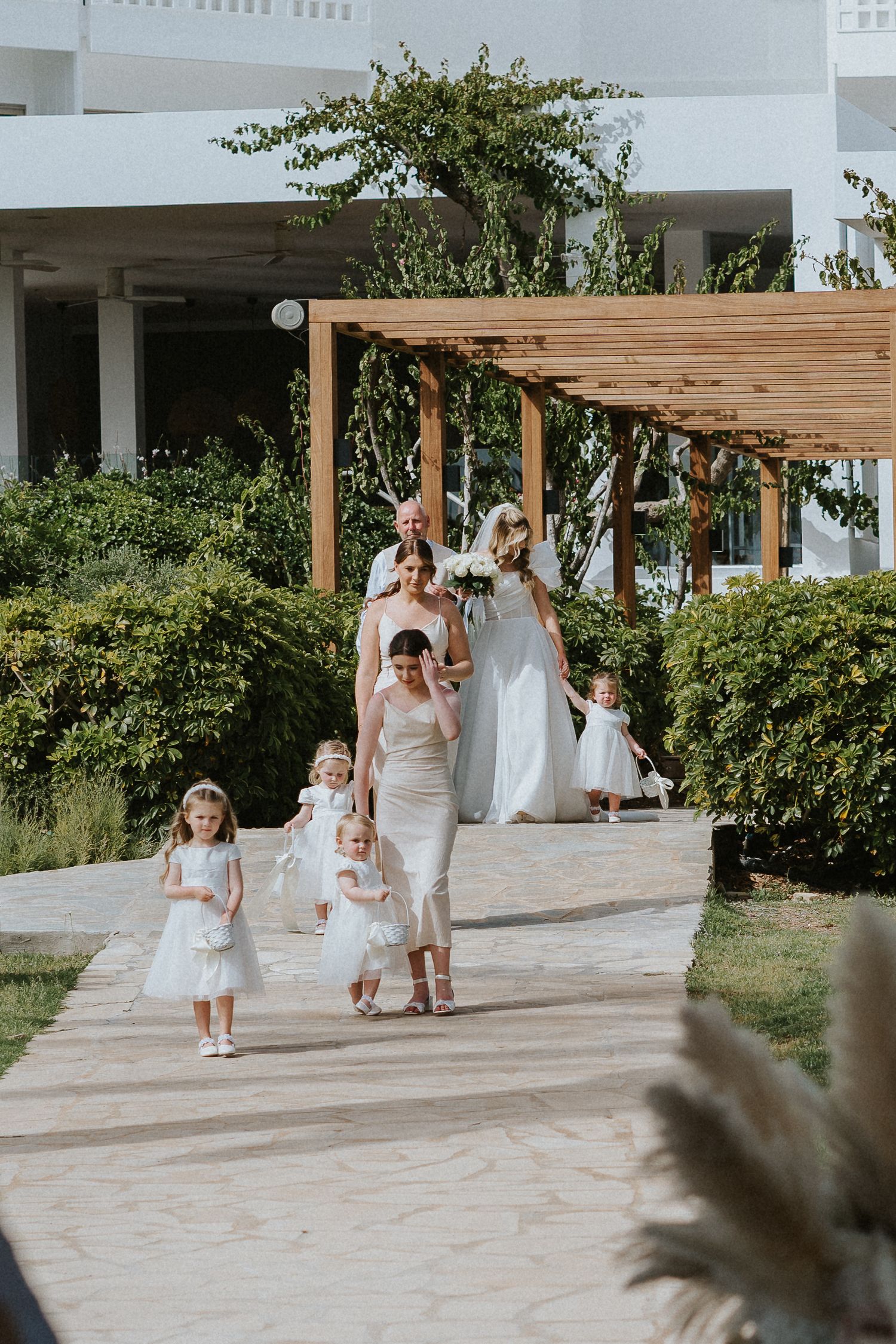 Wedding party walking down a garden path with pergola and lush landscaping.