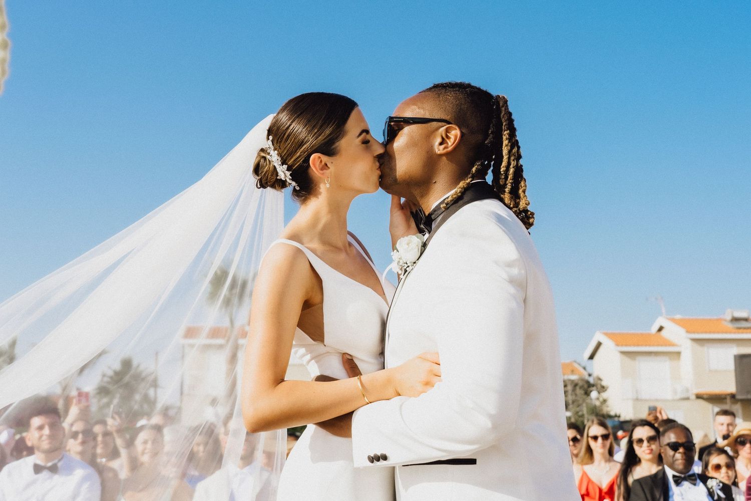 Tender wedding kiss captured against a backdrop of blue sky and palm trees.