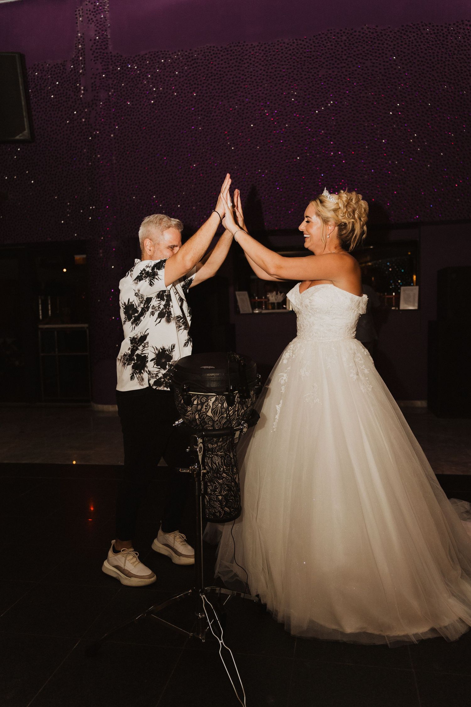 A bride in a white ballgown shares a celebratory high-five moment during a wedding reception.