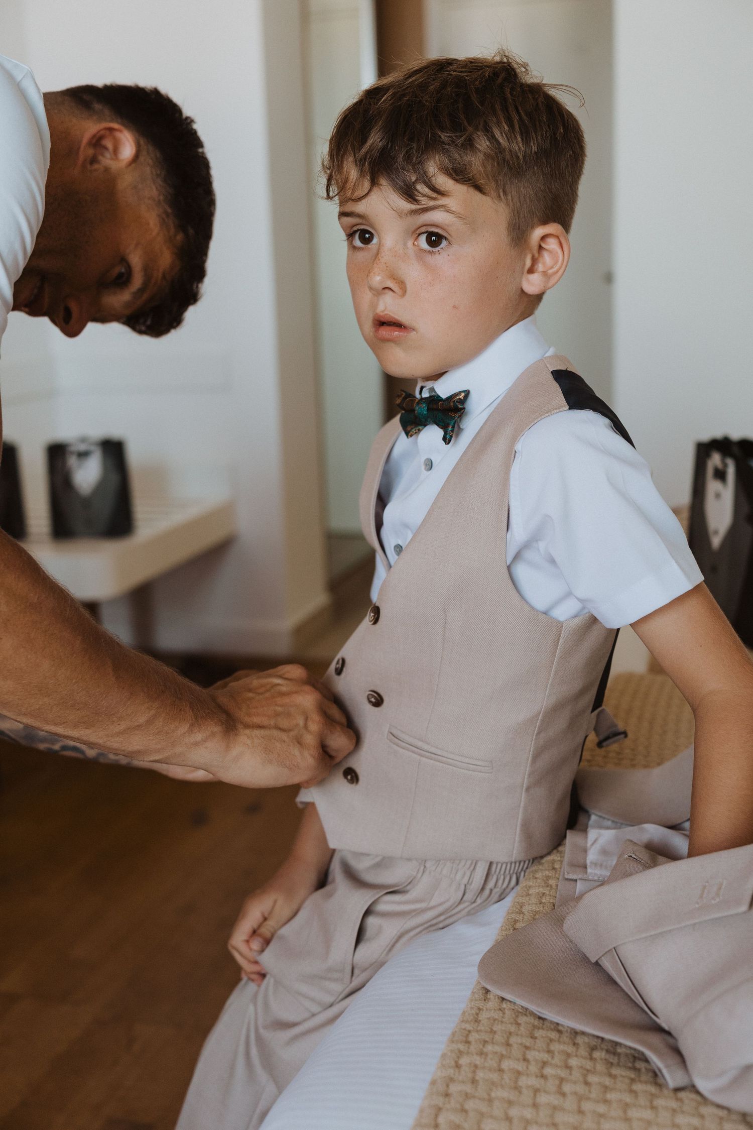 Young ring bearer in beige vest and bowtie getting ready for wedding ceremony.
