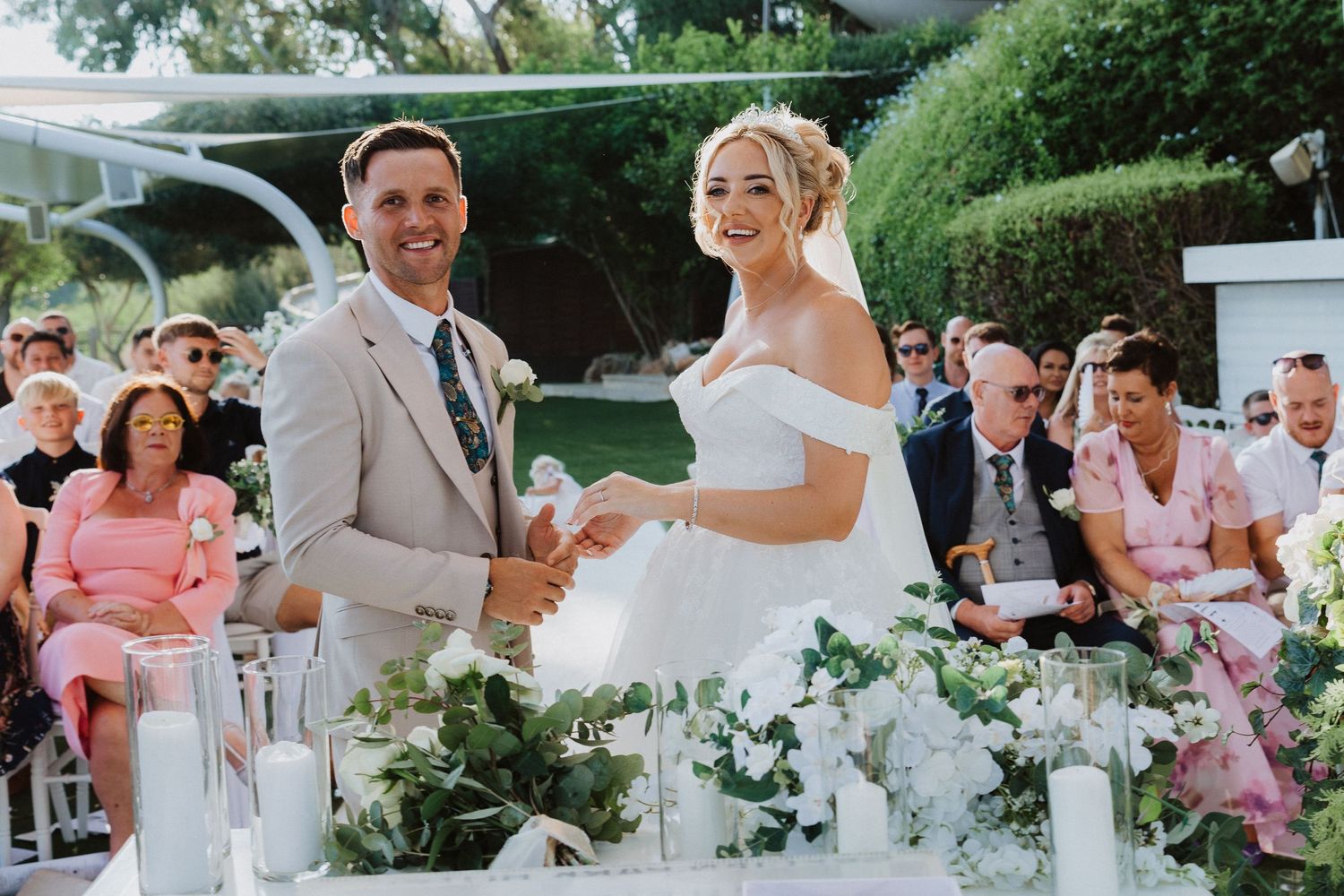Newlyweds share a joyful moment at their outdoor reception with floral centerpieces and seated guests.
