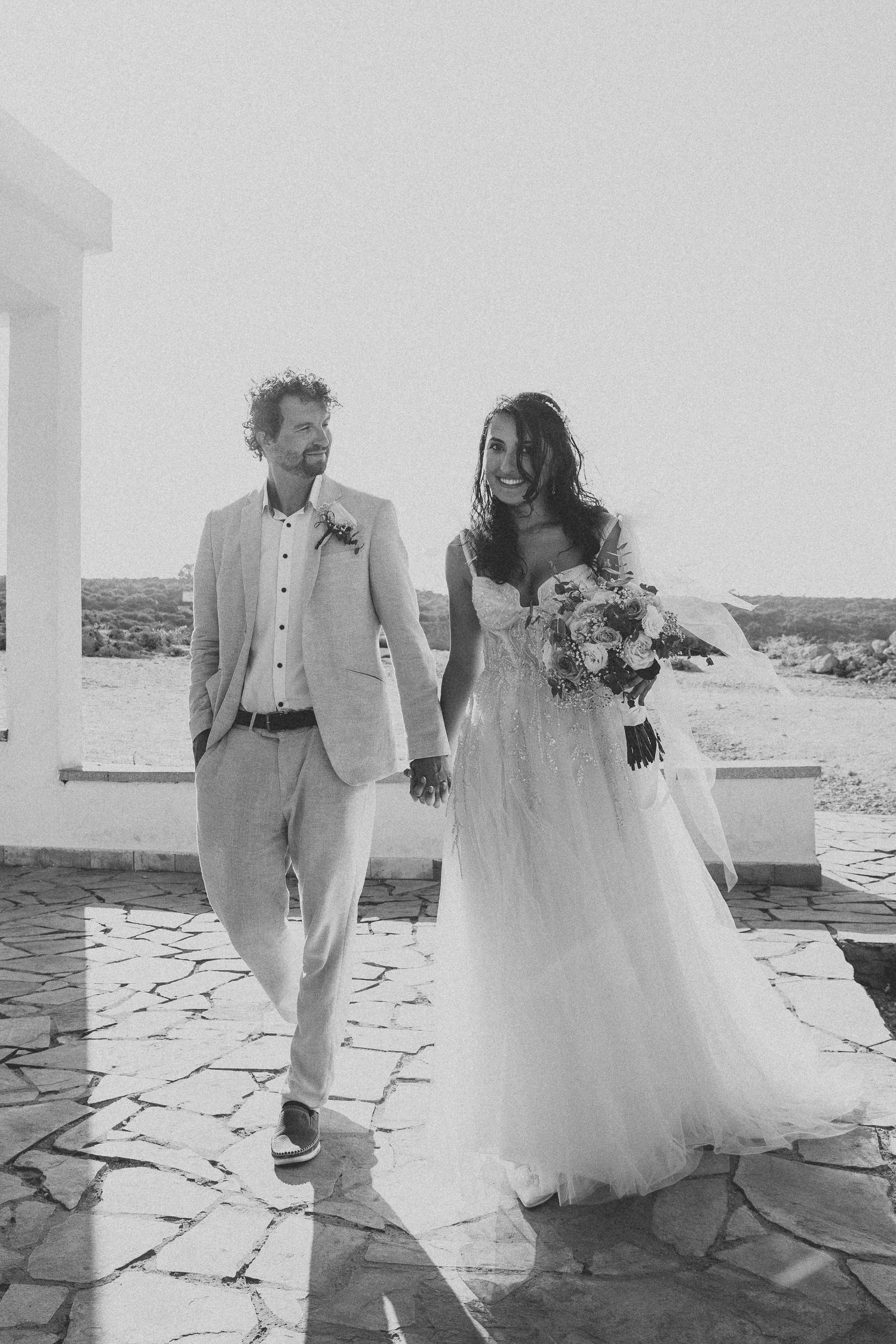 A black and white wedding photo of a couple walking together on a stone path.
