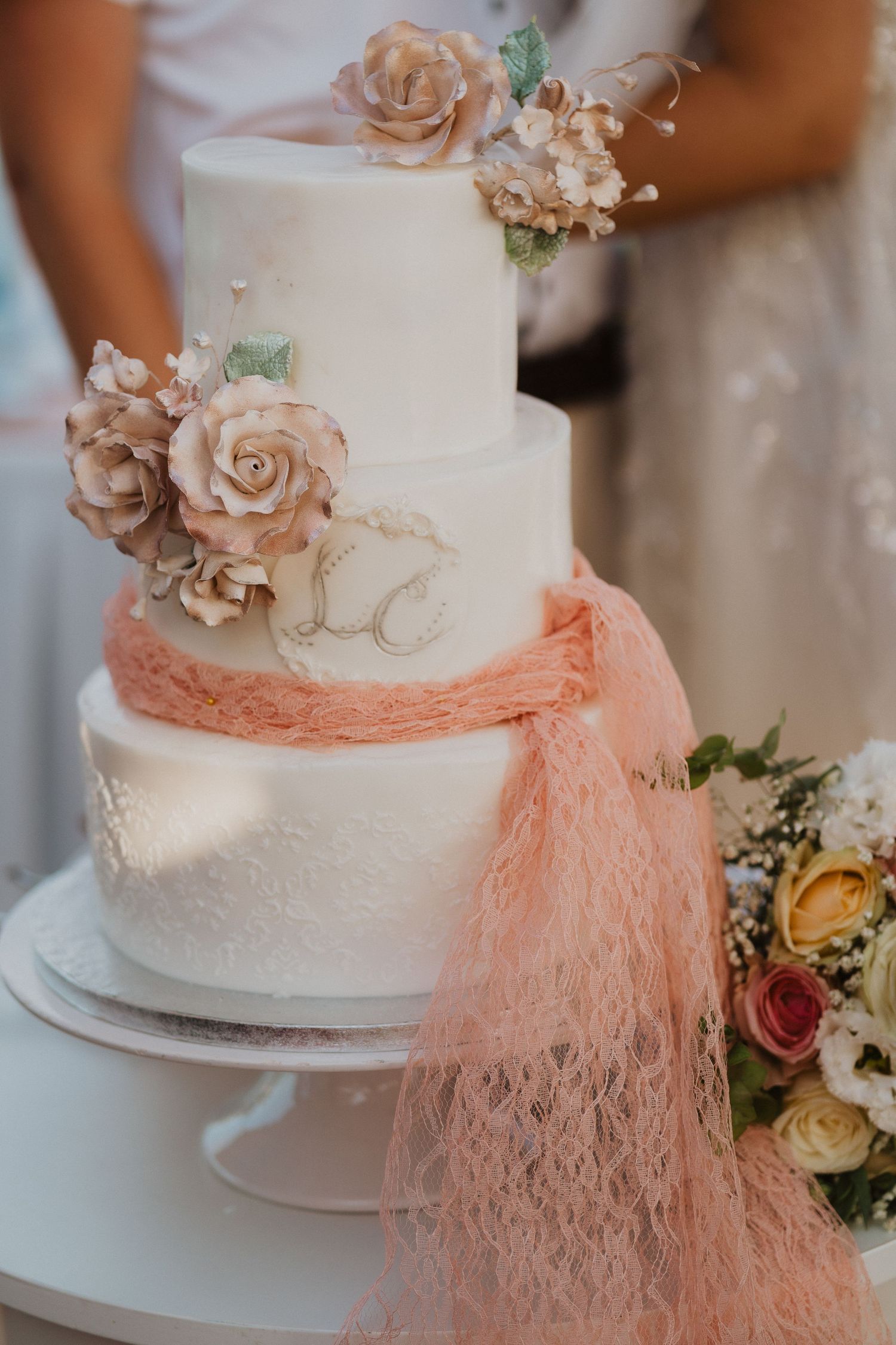 A detailed shot of an elegant white wedding cake with blush roses and coral lace trim.