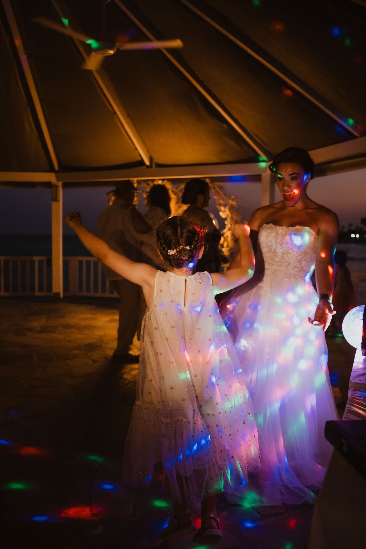 Wedding reception dance floor with colorful disco lights reflecting off white dress.