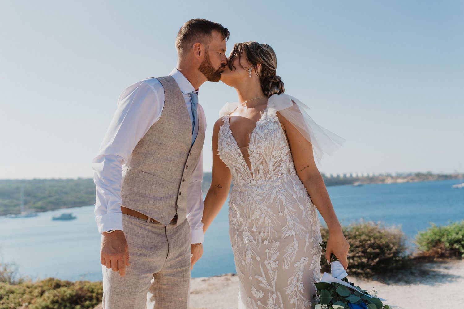 Wedding couple shares tender moment on coastal overlook.