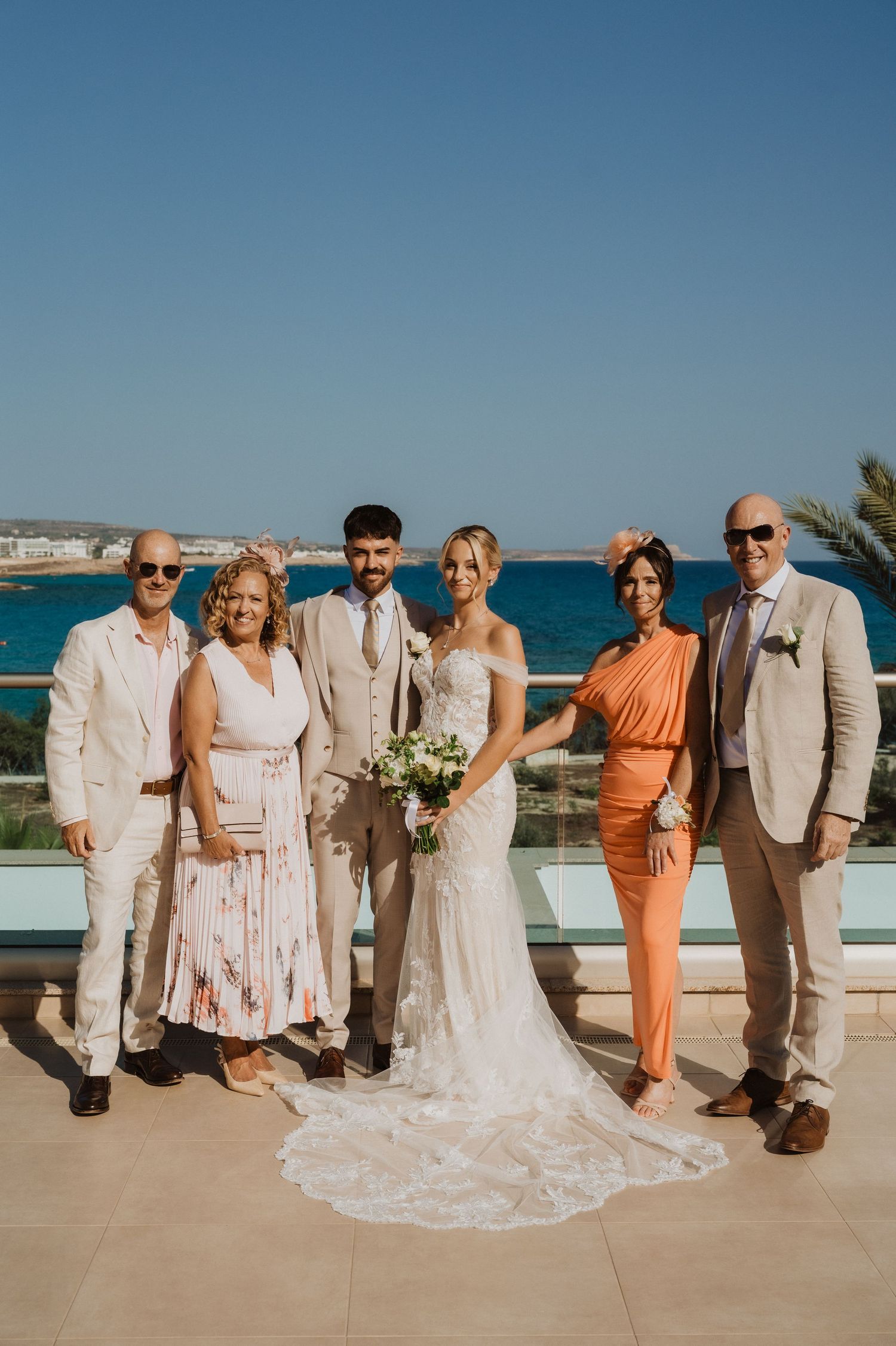 Wedding party poses on a terrace overlooking bright blue ocean waters.