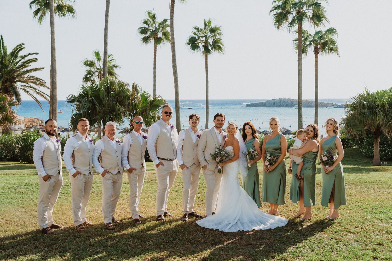 Wedding party lined up for photos with palm trees and ocean backdrop.