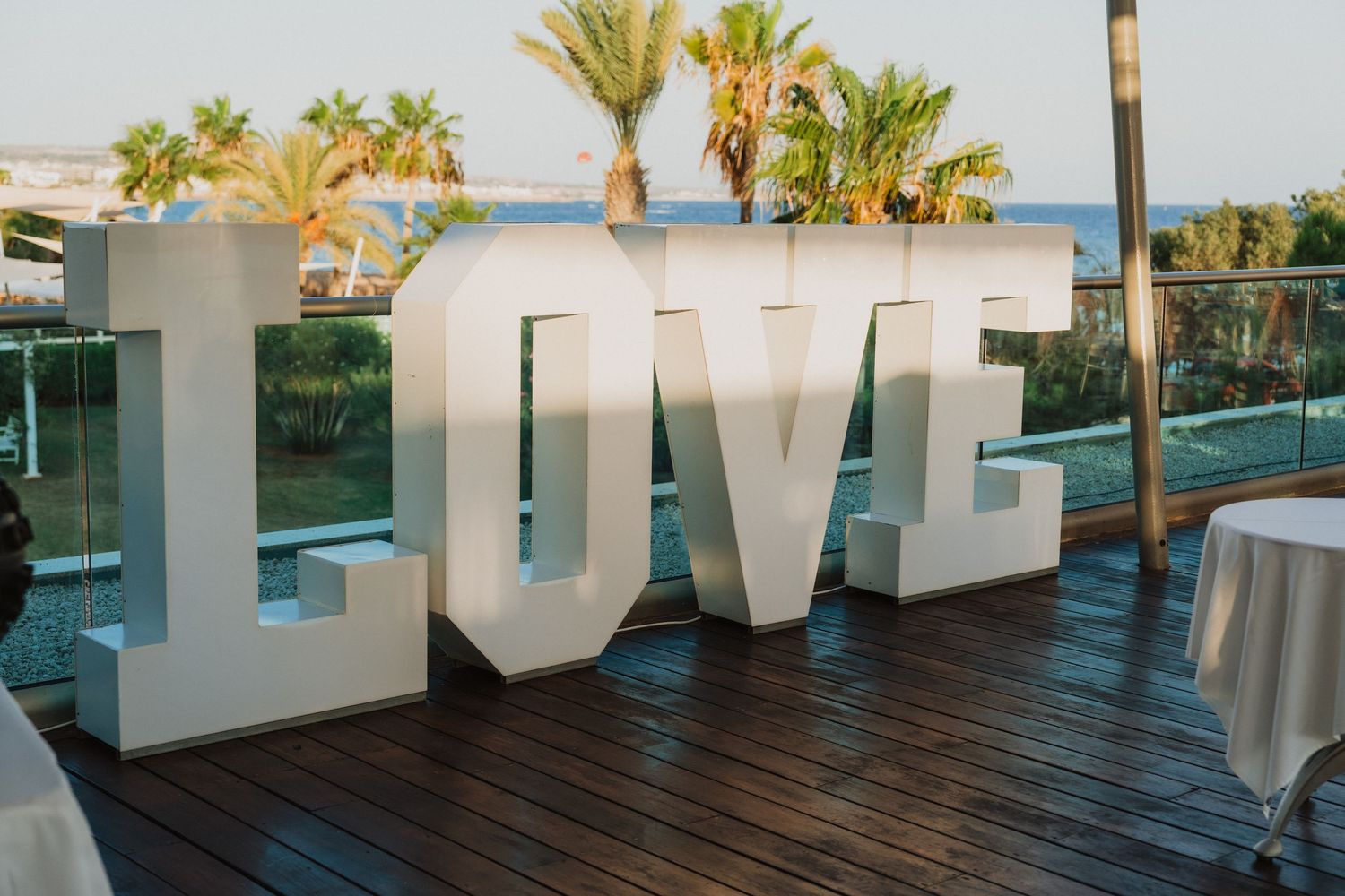 Large white LOVE letters displayed on a wooden deck with palm trees and ocean views at a beach wedding venue.