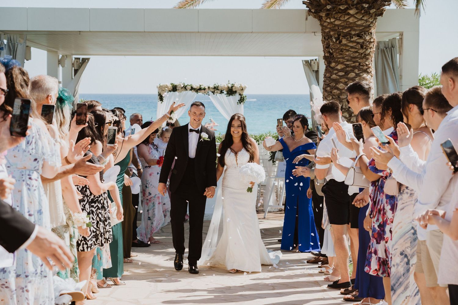 Wedding party and guests celebrate on covered seaside patio.