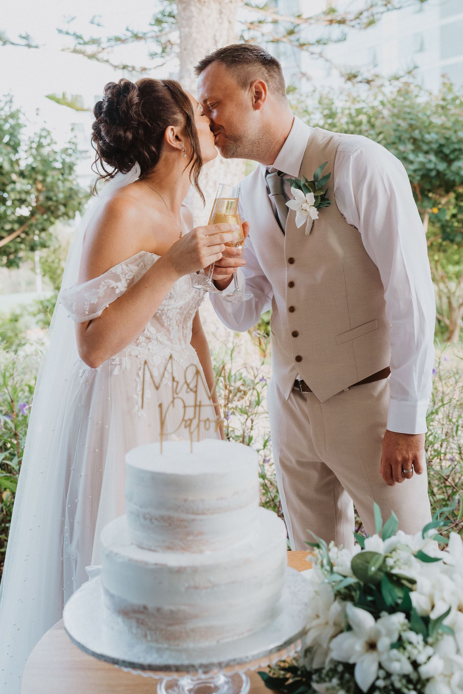 A romantic wedding moment with champagne glasses and a three-tiered white cake decorated with 'Mr & Mrs' signage.