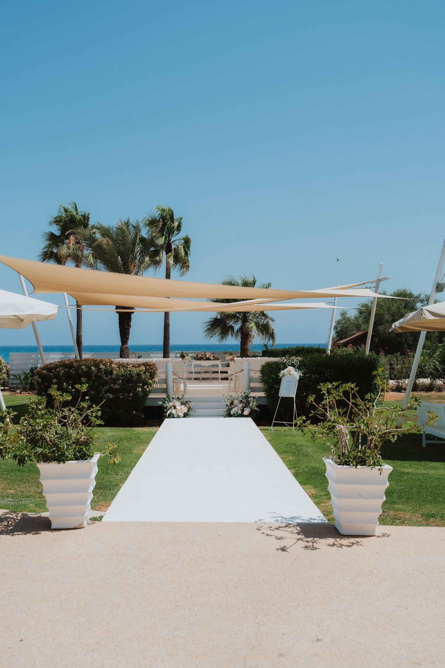 Beachfront wedding ceremony setup with white aisle and tan shade sails overlooking the ocean.