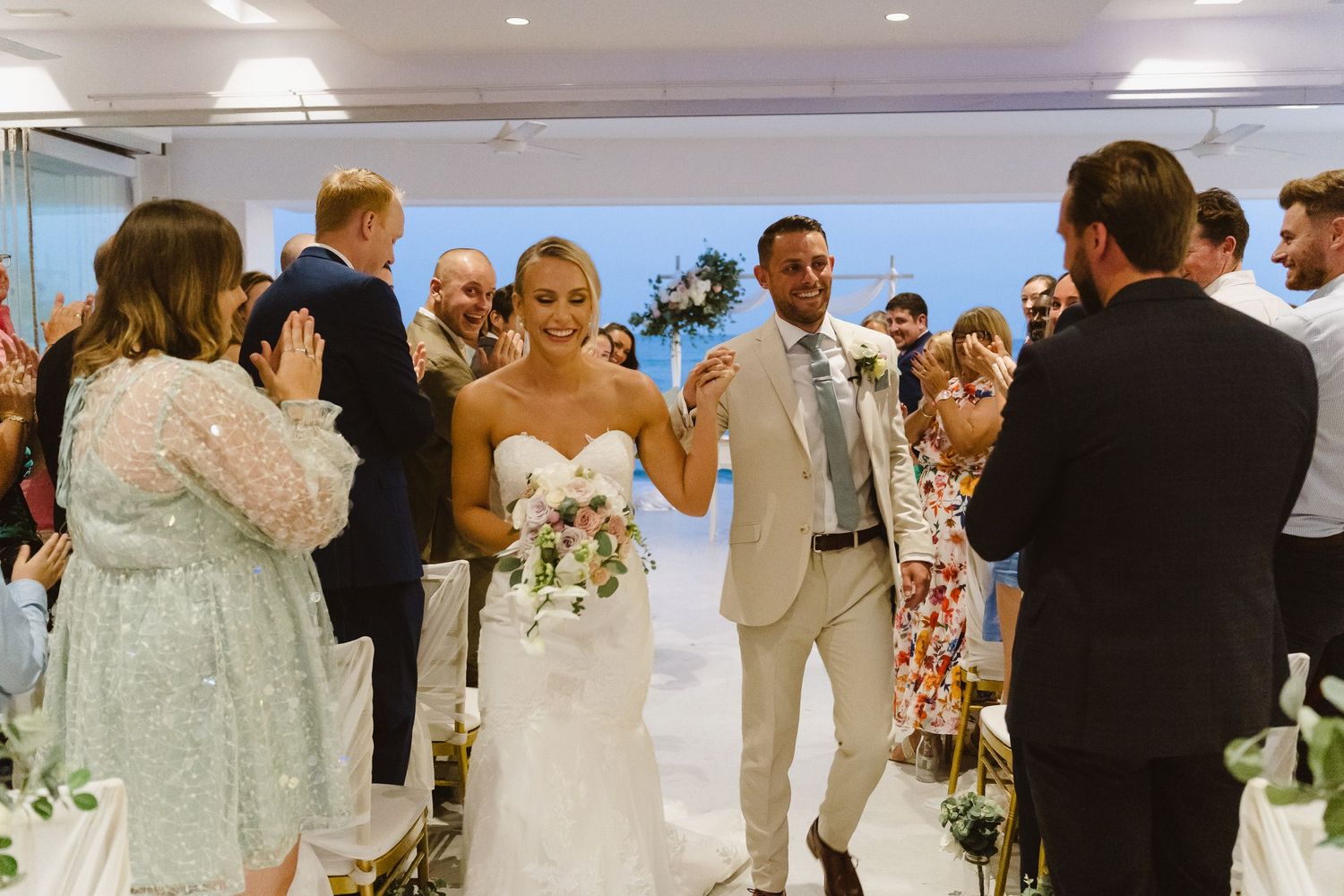Wedding couple walks down aisle while guests in formal attire celebrate their union.