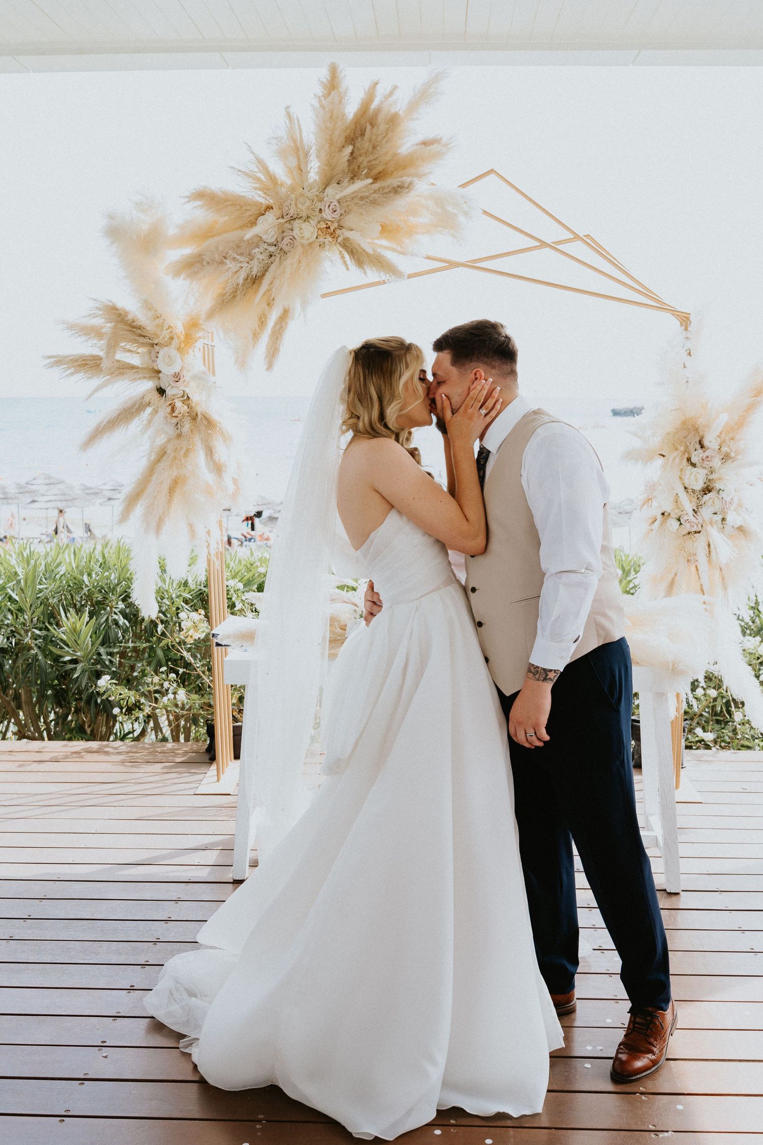 Romantic moment under pampas grass arch at beachfront wedding venue.