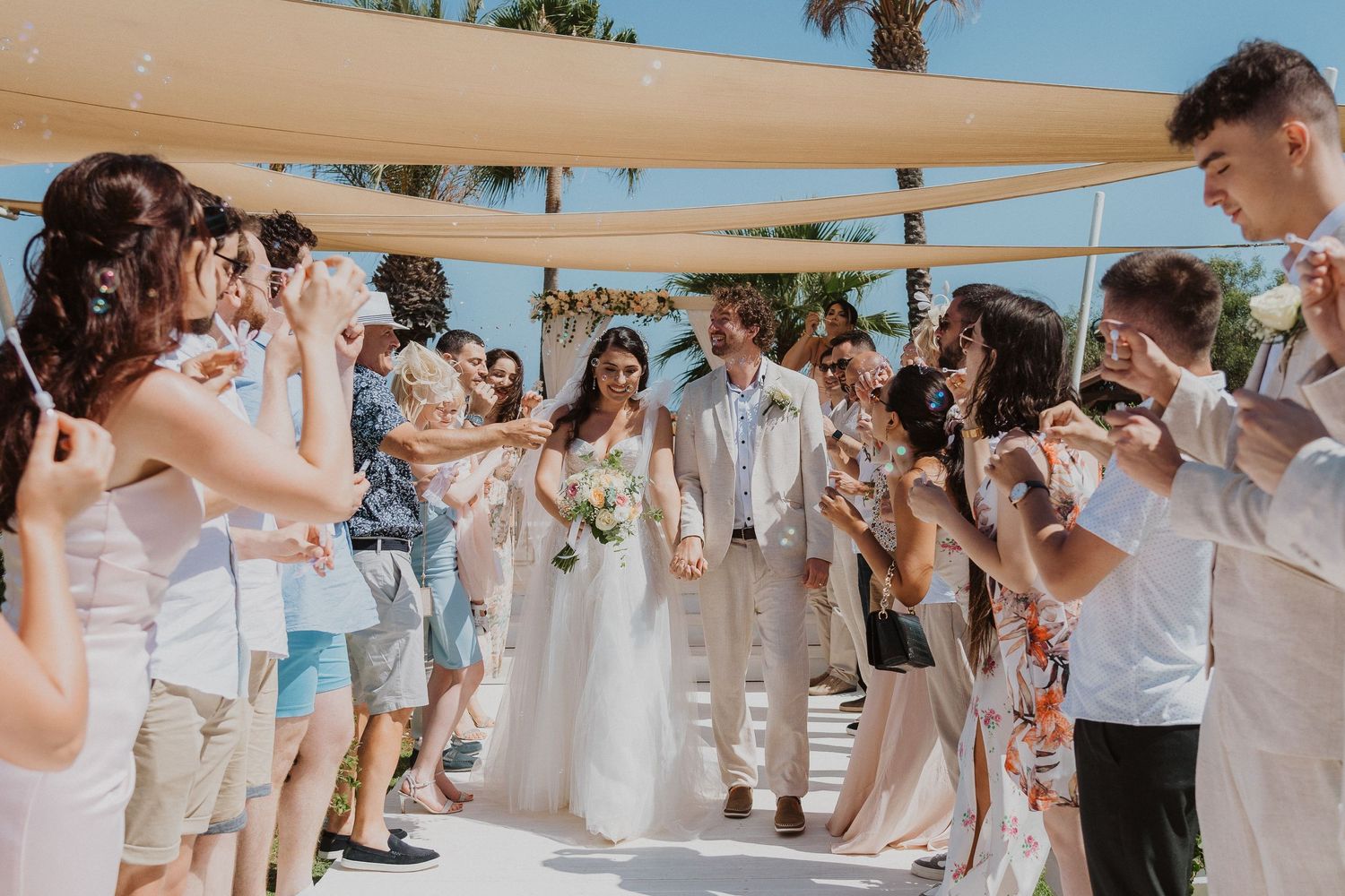 Wedding guests line walkway blowing bubbles as newlyweds walk through outdoor ceremony.
