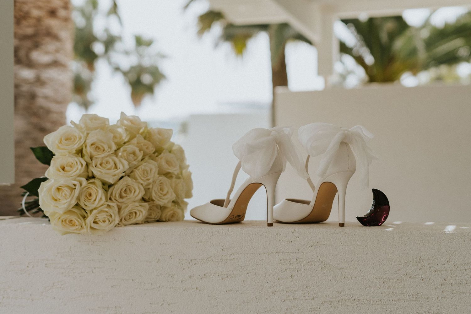 Elegant white bridal shoes and cream rose bouquet on light colored surface.