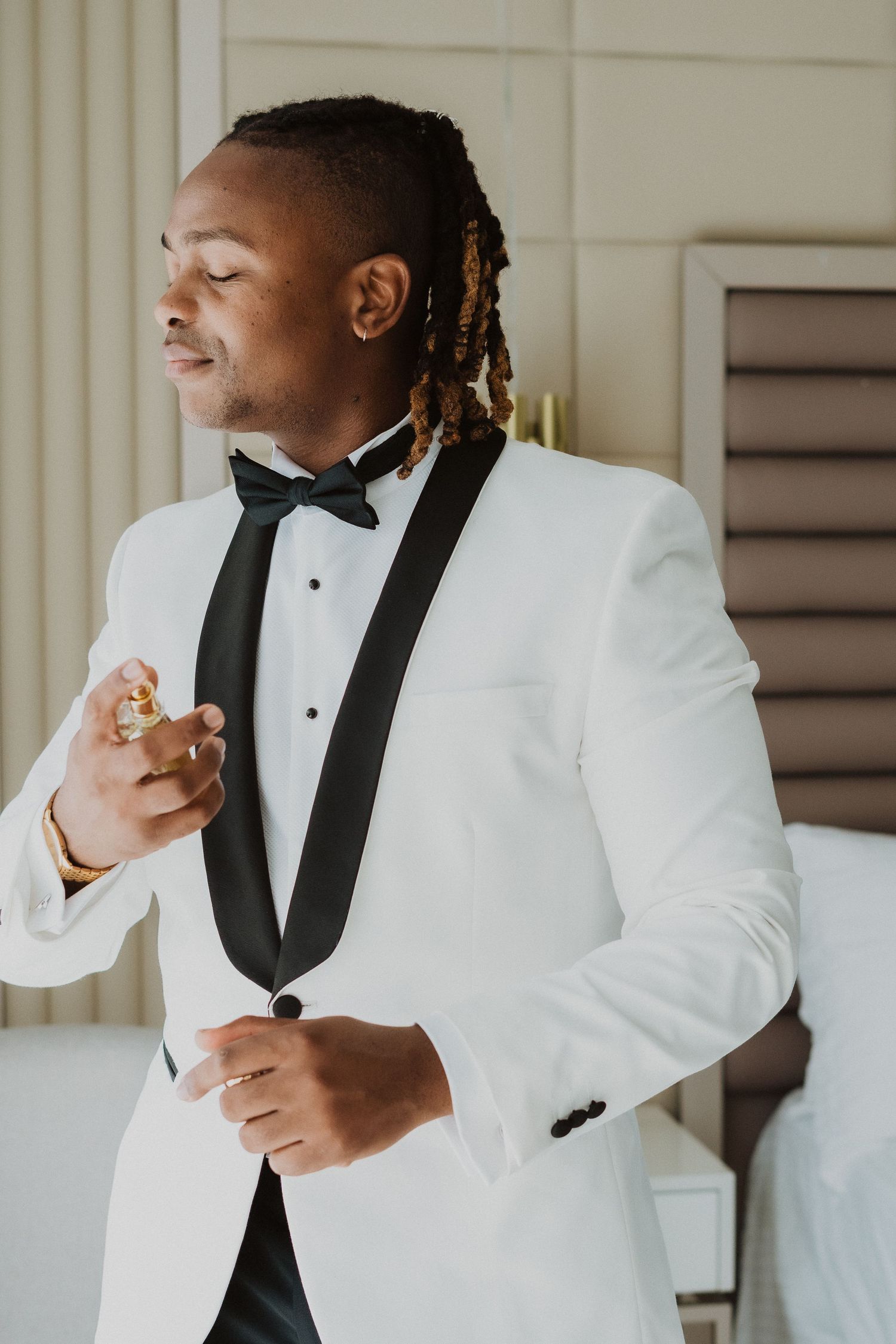 A person in a white tuxedo adjusts their bowtie while getting ready.