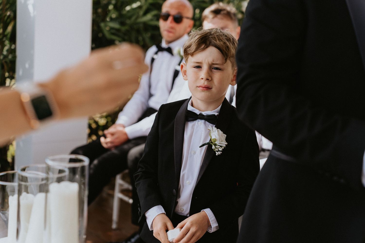 Young ring bearer observing wedding ceremony while standing next to adults.
