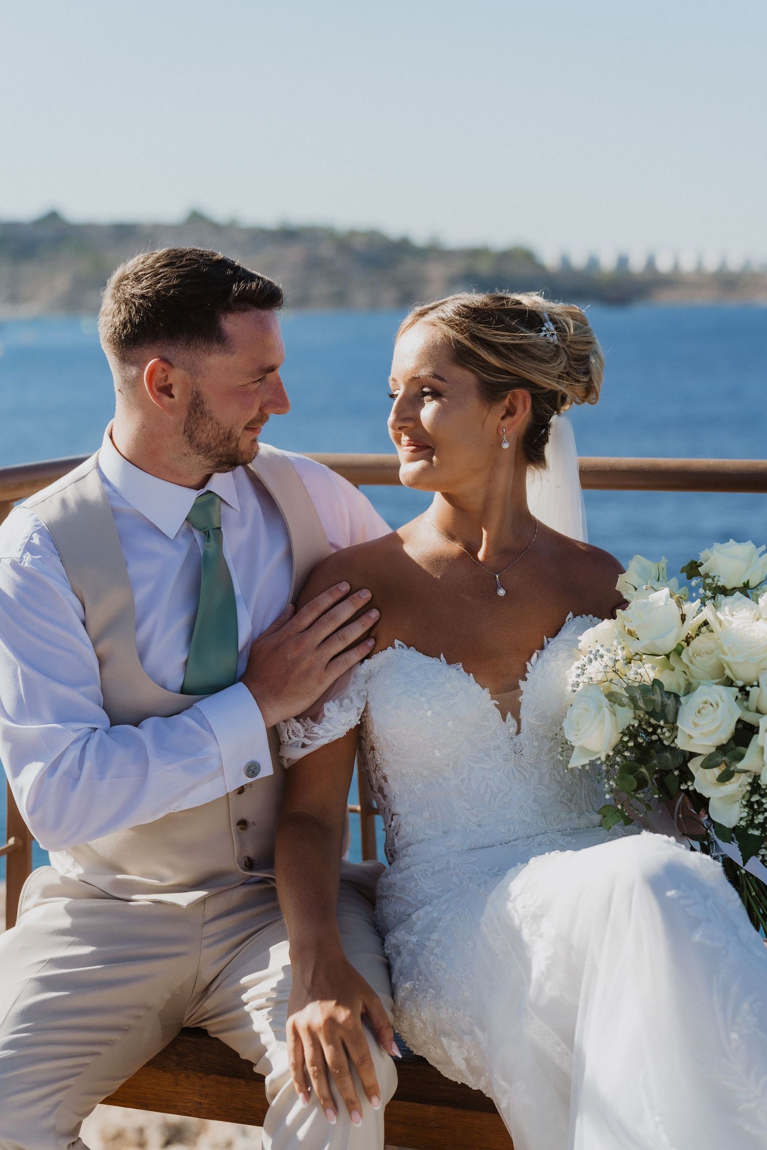 Newlywed couple shares an intimate moment on a boat deck with ocean views and white floral bouquet.