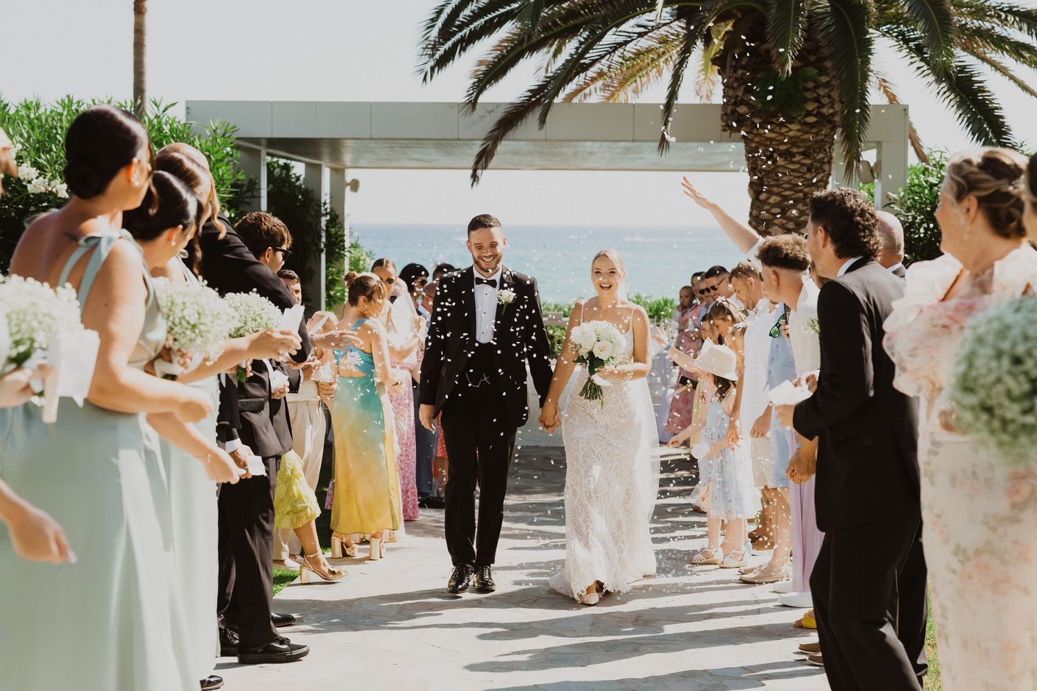 Wedding party lined up outdoors with palm trees and bridesmaids in light blue dresses.