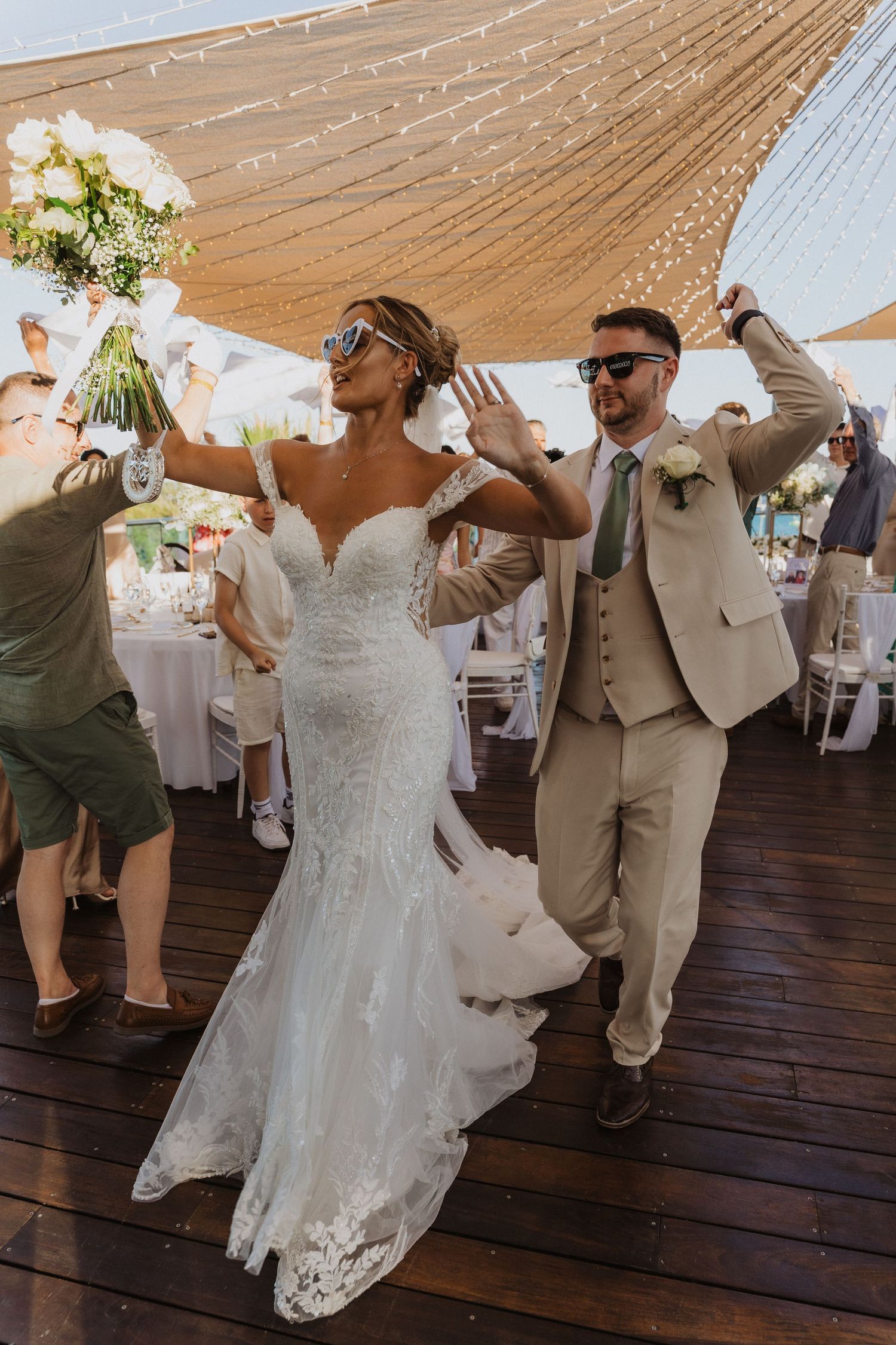 Newlywed couple dances together on wooden floor under draped tent during wedding reception celebration.