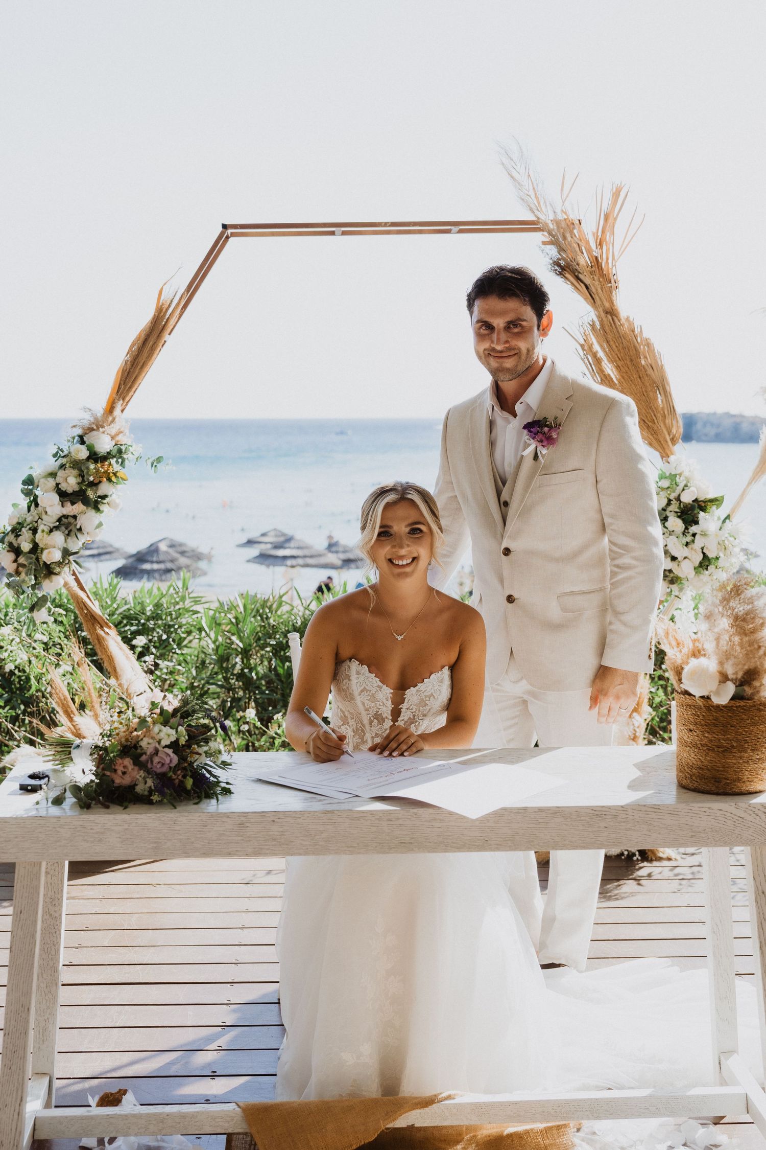 Couple signing marriage documents at a beachside venue with wheat decor and floral arrangements.