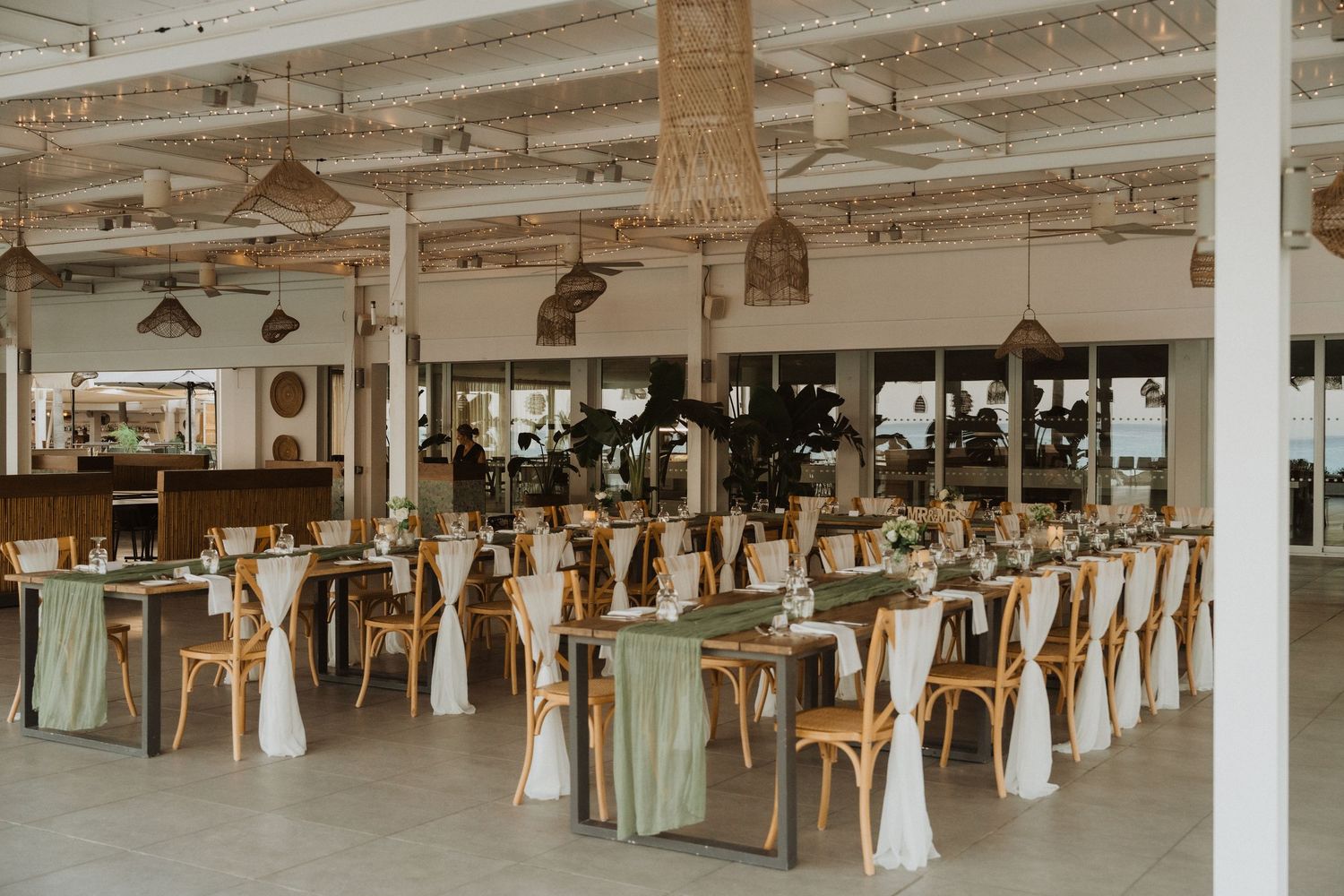 Spacious wedding venue interior with rows of decorated tables and industrial-style ceiling.